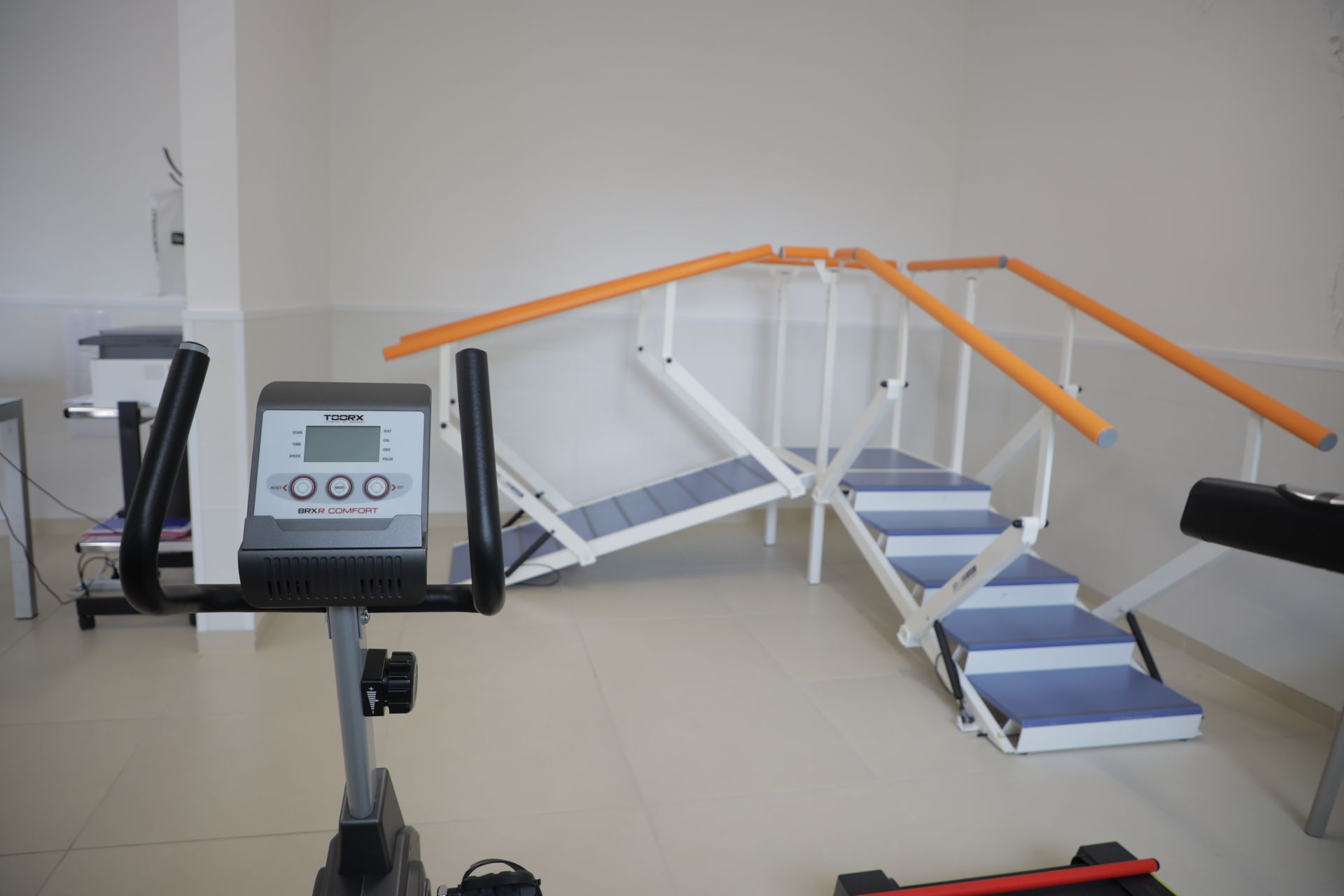 Una sala di fisioterapia con una cyclette stazionaria in primo piano e una scalinata per esercizi con corrimano.