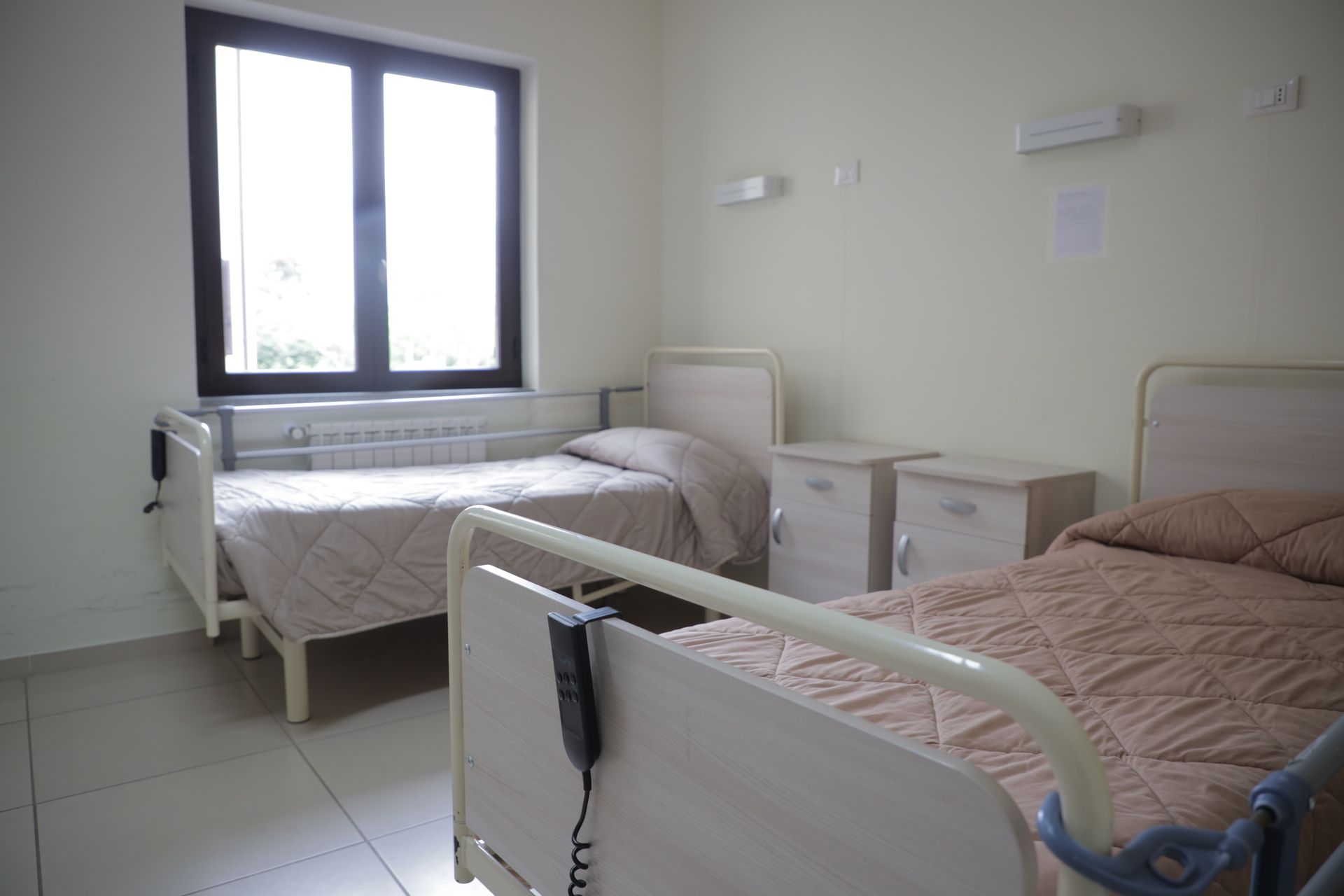 Una camera d'ospedale pulita e minimalista con due letti con copriletti trapuntati beige, telai bianchi e comodini abbinati.