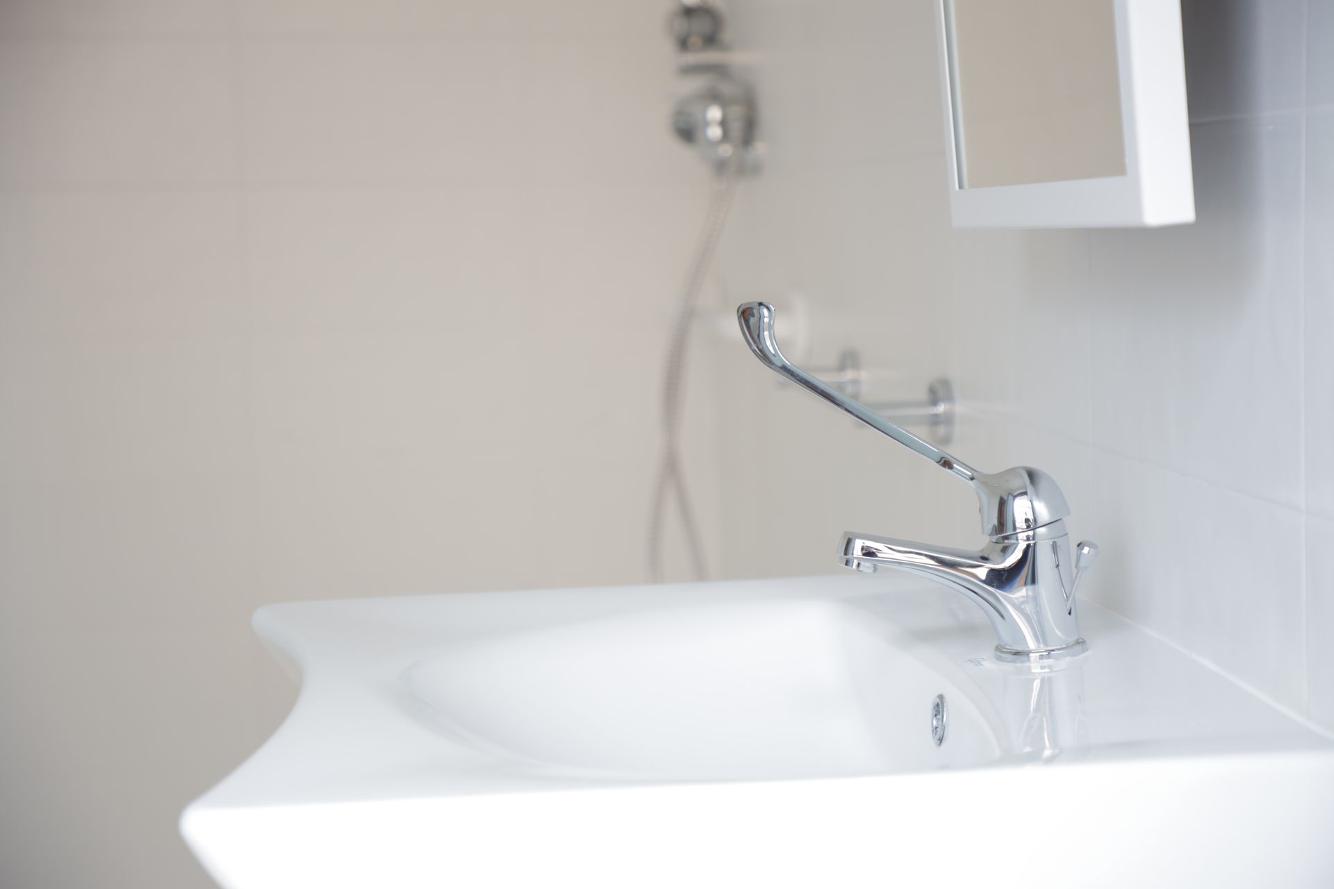 Un lavabo bianco da bagno con un moderno rubinetto cromato e un soffione doccia visibile sullo sfondo sfocato.