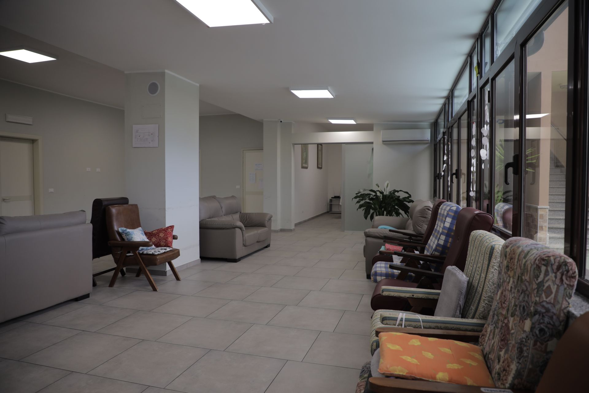 Una luminosa sala d'attesa piastrellata con diverse poltrone disposte lungo una parete finestrata e un divano più arretrato.