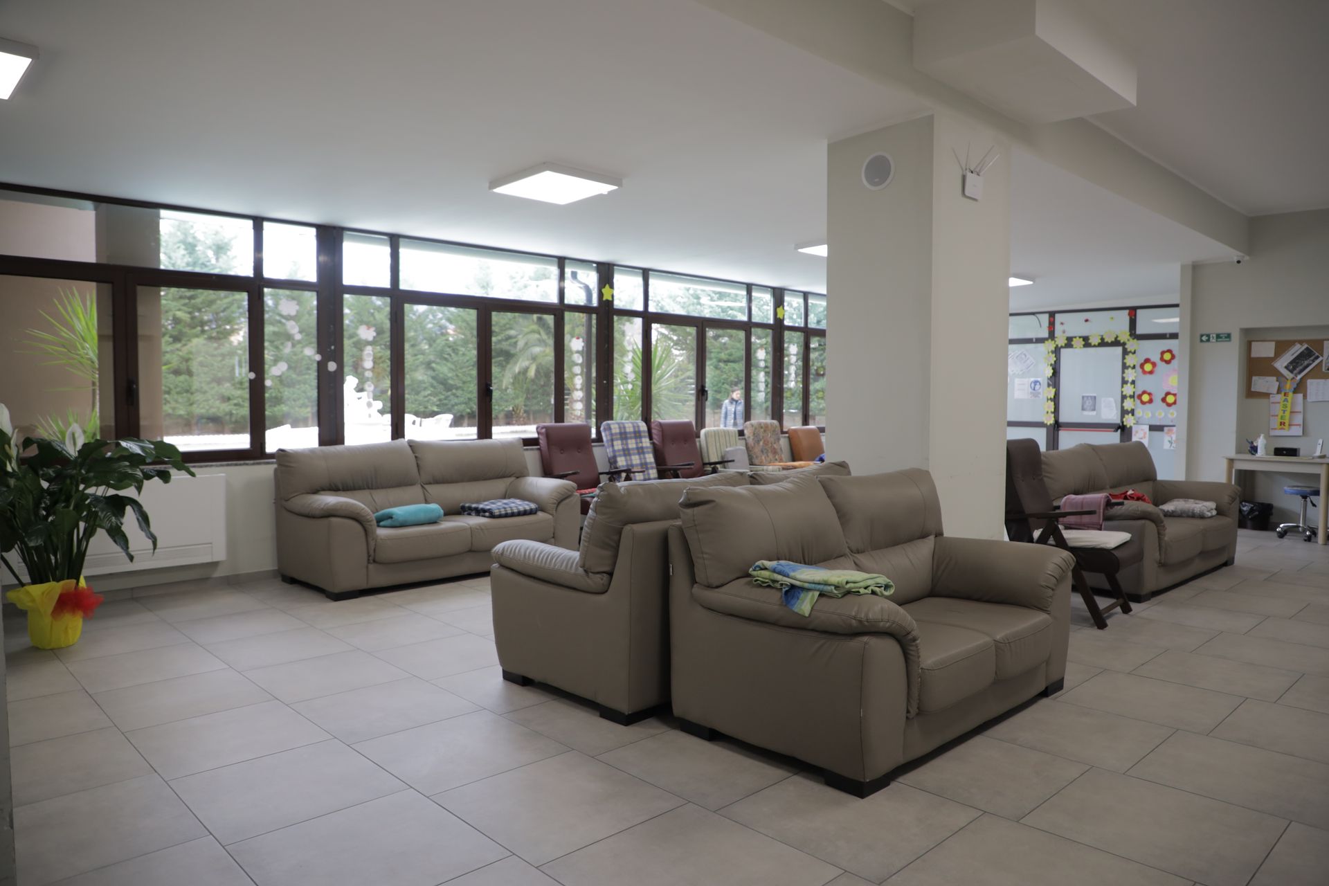 Un'ampia hall con divani beige, pavimenti piastrellati, grandi finestre e una pianta in vaso.