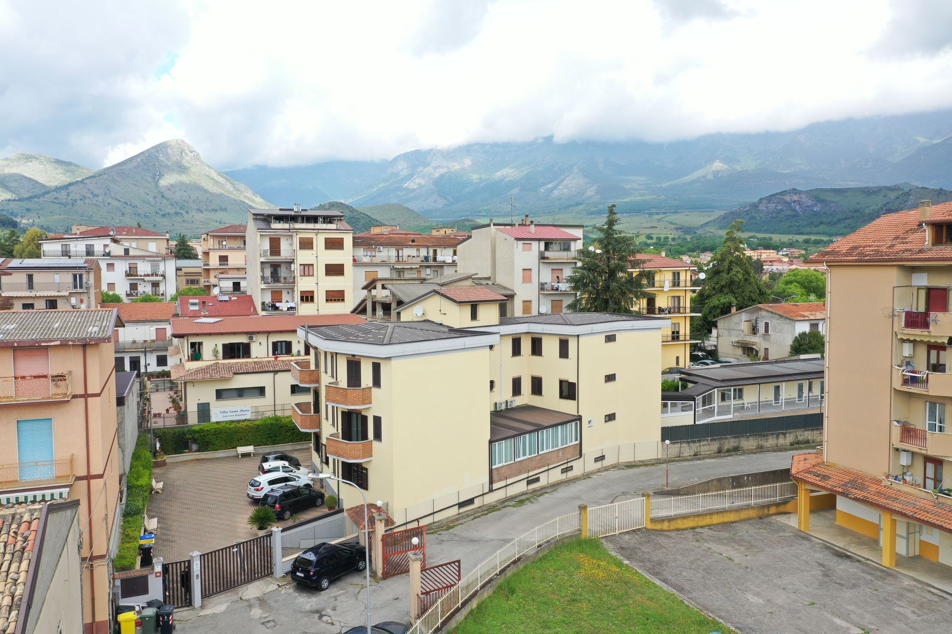 Un quartiere residenziale con palazzi di colore chiaro sotto un cielo nuvoloso, con le montagne sullo sfondo.