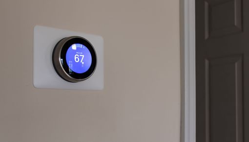 Round digital thermostat on a beige wall near a doorway, displaying 67° in blue.