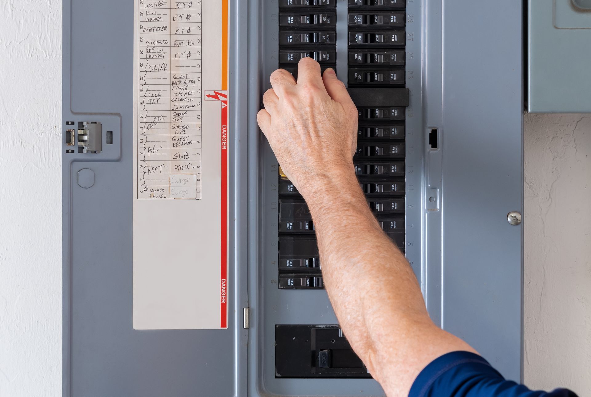 Hand turning a breaker in an electrical panel with a circuit directory on the door