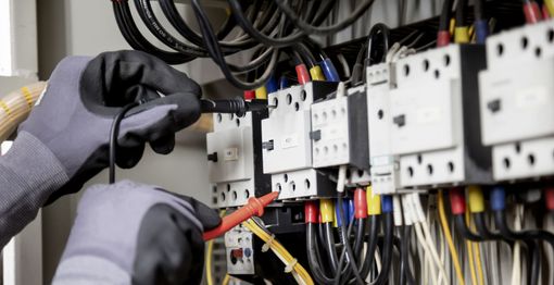 Gloved hands wiring electrical components in a control panel with cables and circuit breakers
