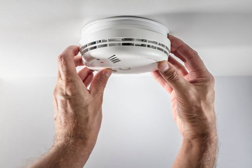 Hands installing a white smoke detector on a ceiling