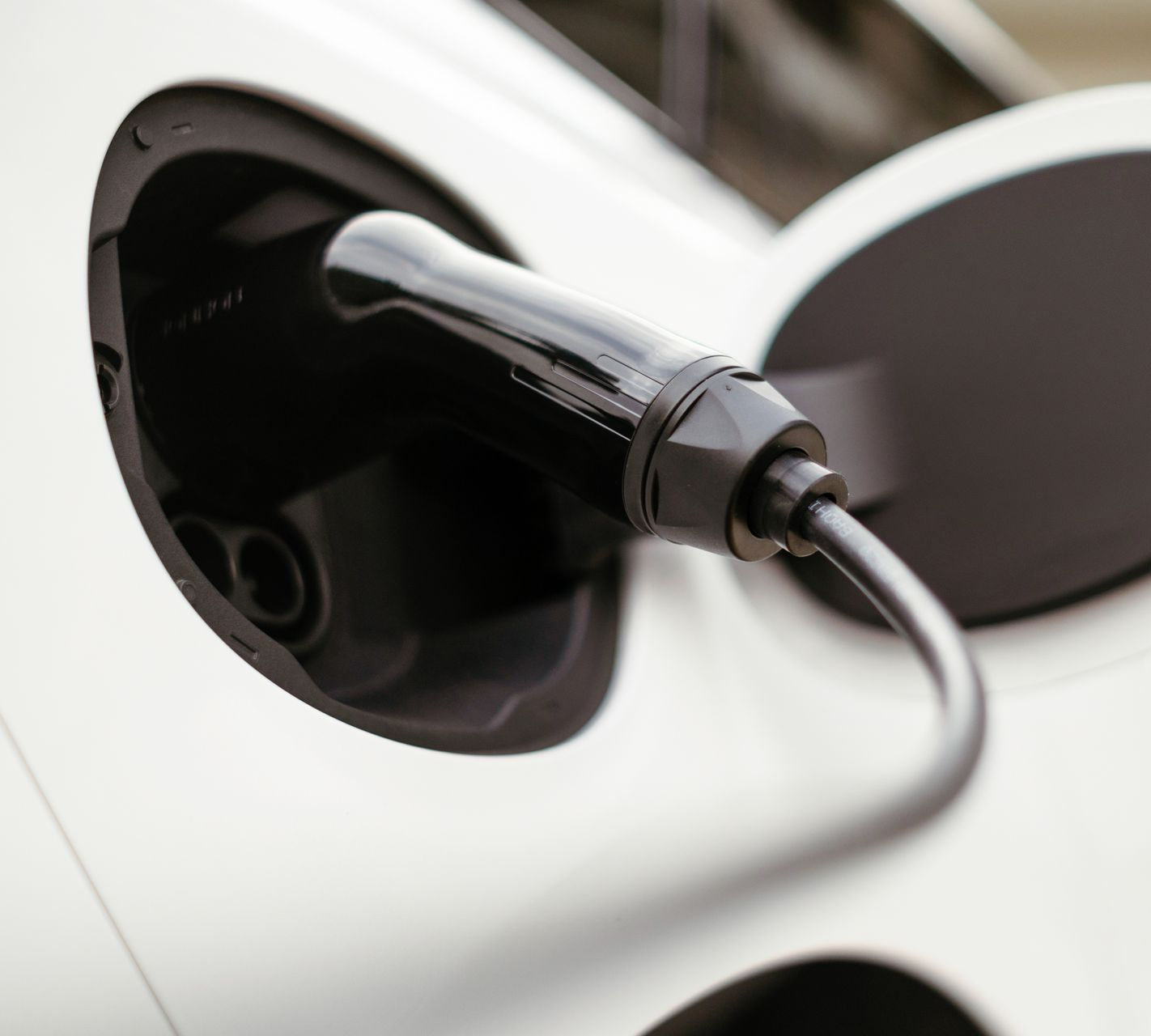 Black electric vehicle charging plug inserted into a white car charging port