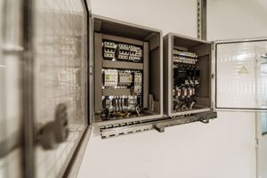 Open electrical panels with wiring and circuit breakers on a white wall