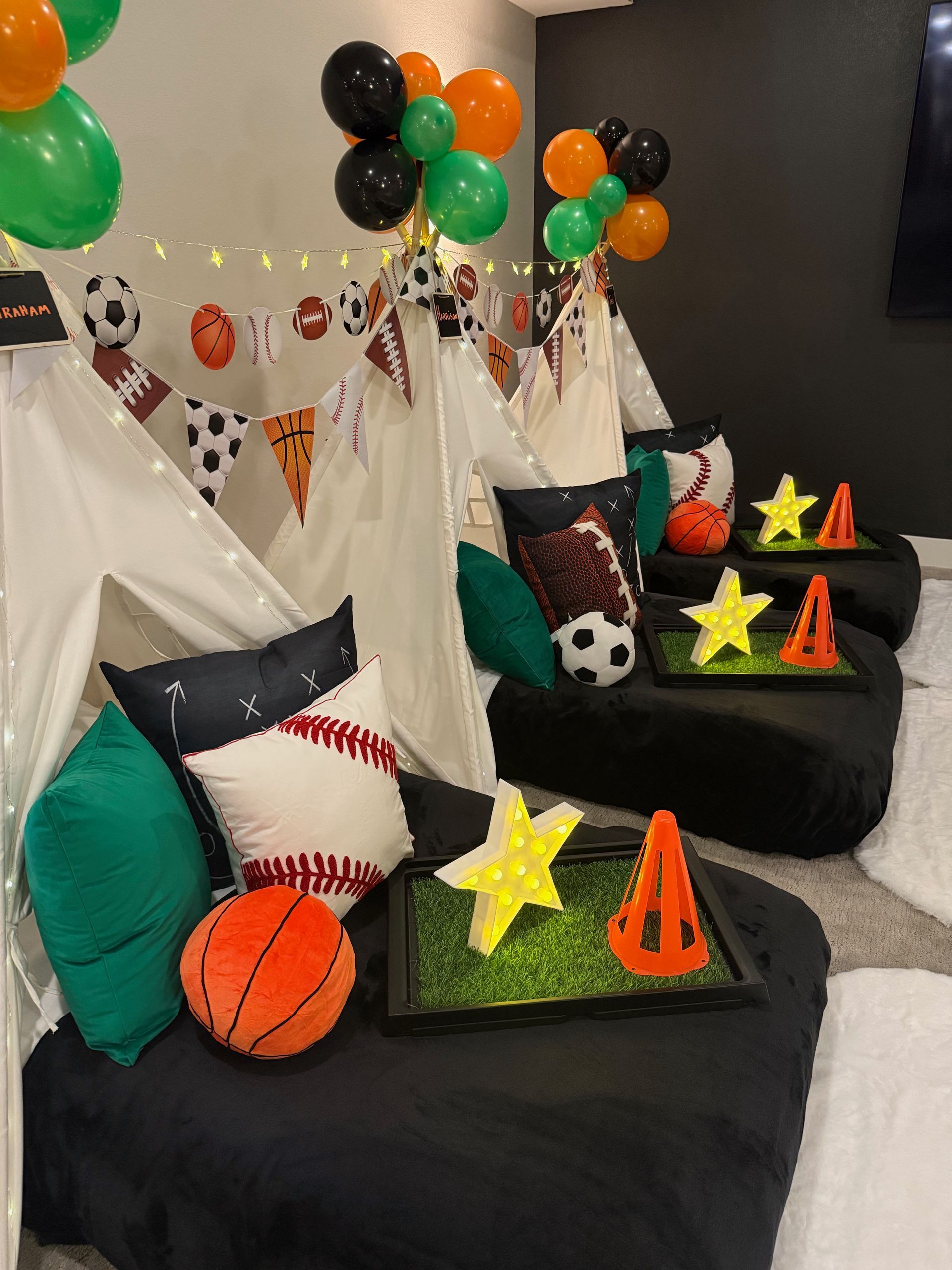 Decorated teepee tent beds with black, orange, and green sport accents, balloons, and pillows