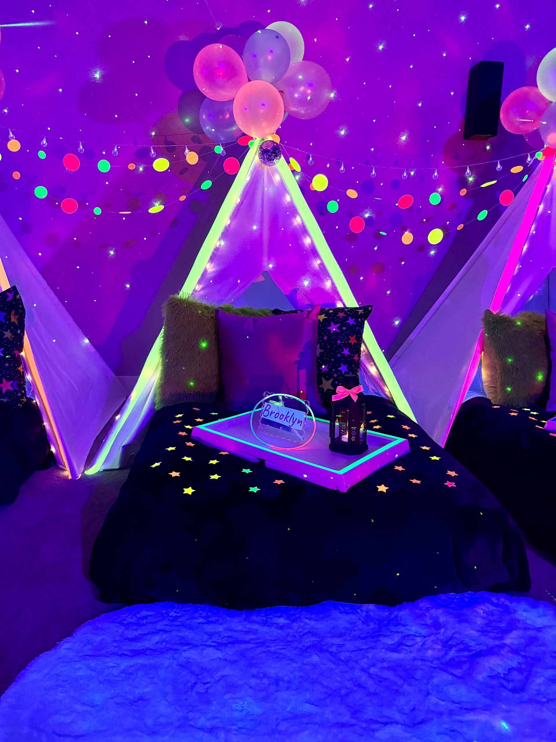 Neon glow-in-the dark party setup with glowing teepee tent beds, balloons, and black light