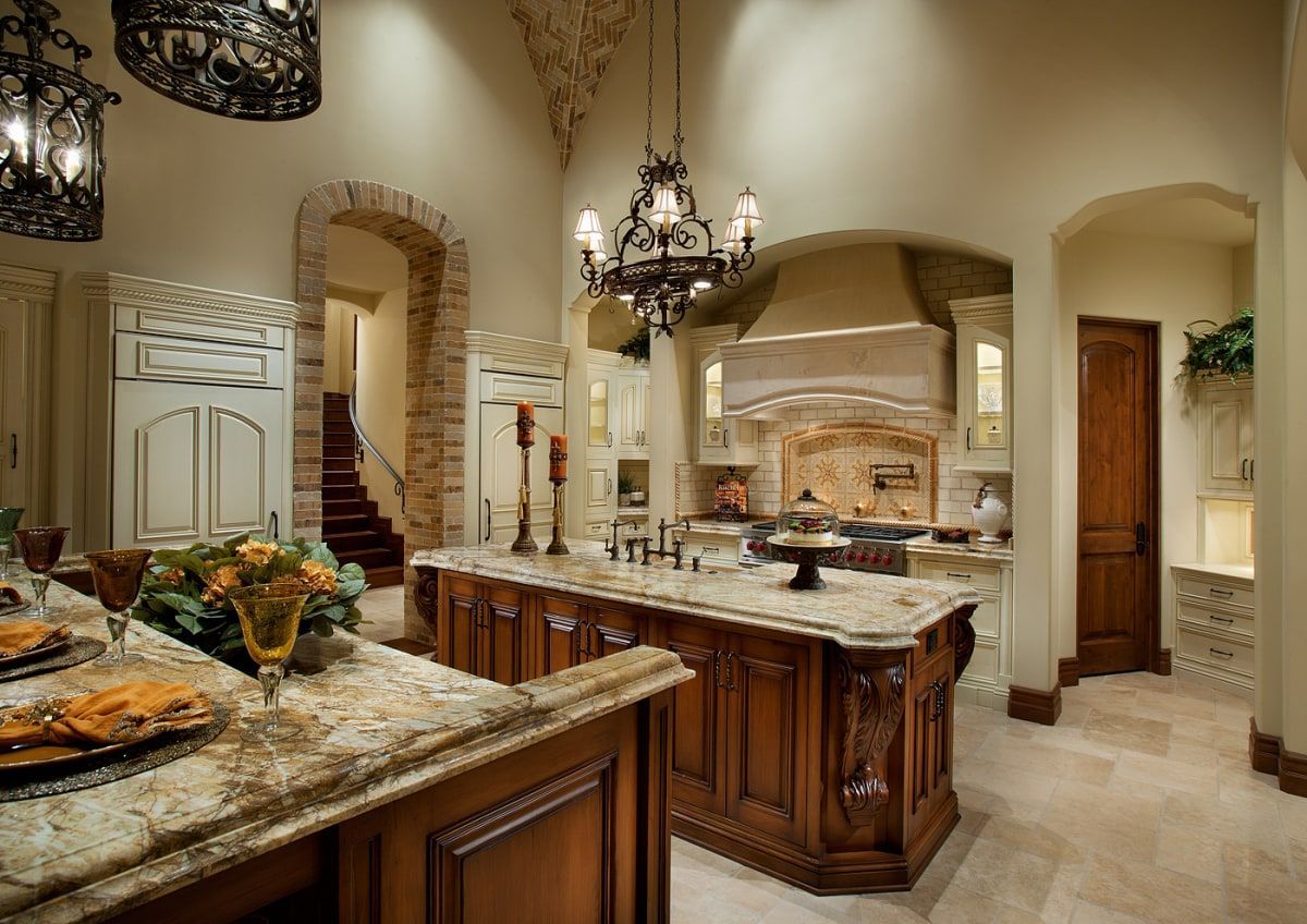 Luxurious kitchen with two wooden islands, granite countertops, and ornate chandeliers.