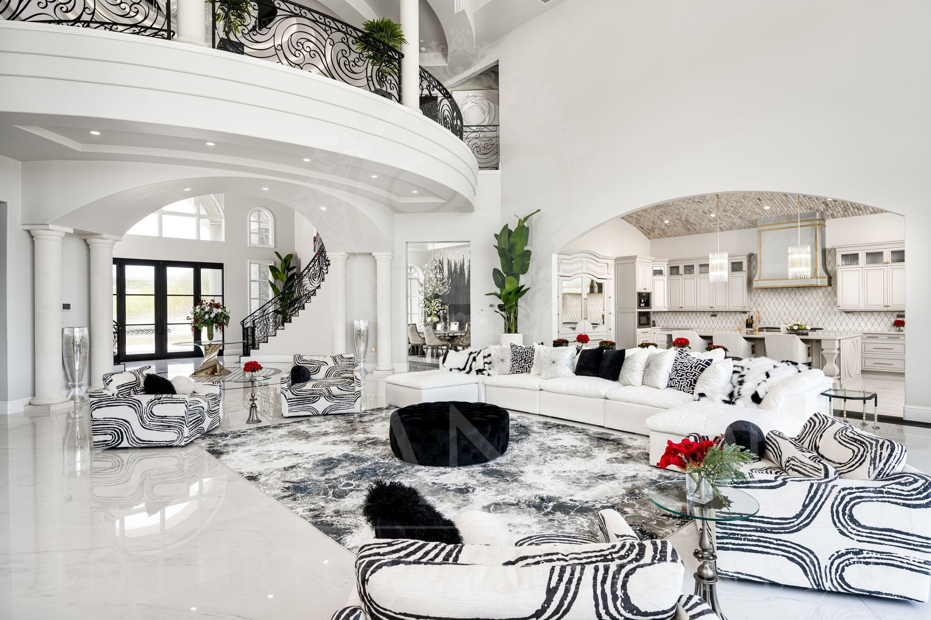 Spacious white living room with black and white patterned furniture, a curved staircase, and open kitchen in the background.