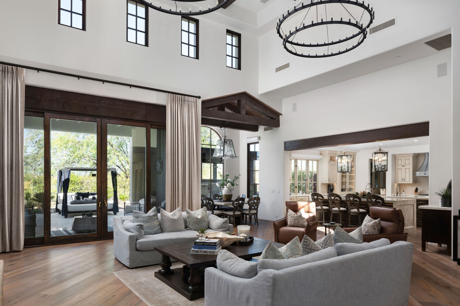 Spacious living room with light wood floors, sofas, and large windows leading to an outdoor space.