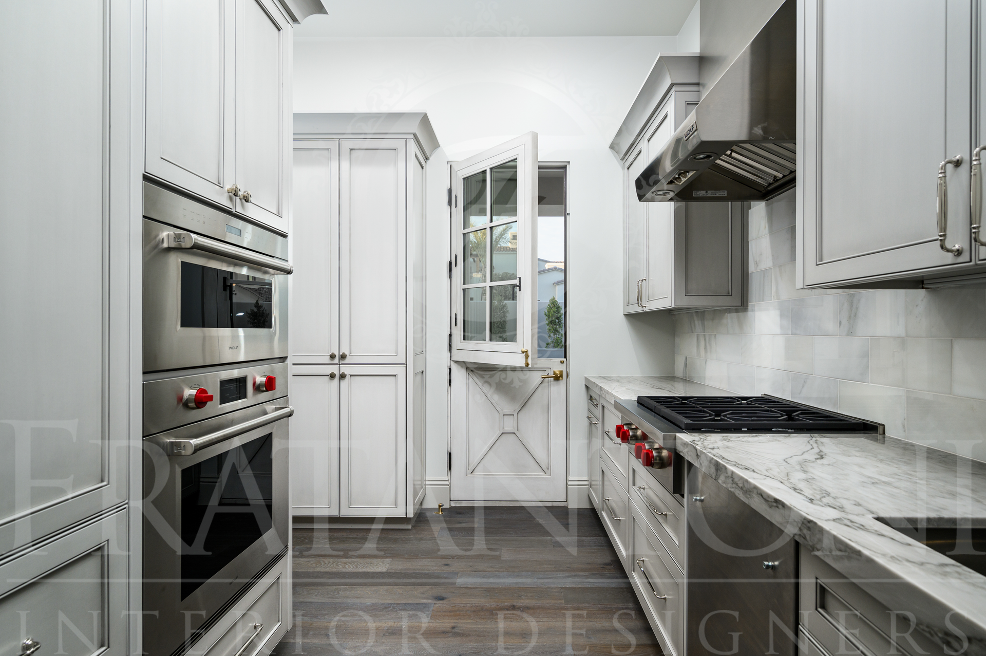 Luxury butlers pantry with white cabinets, marble counters, stainless appliances, and a dark wood floor designed by luxury interior designers Fratantoni Interior designers