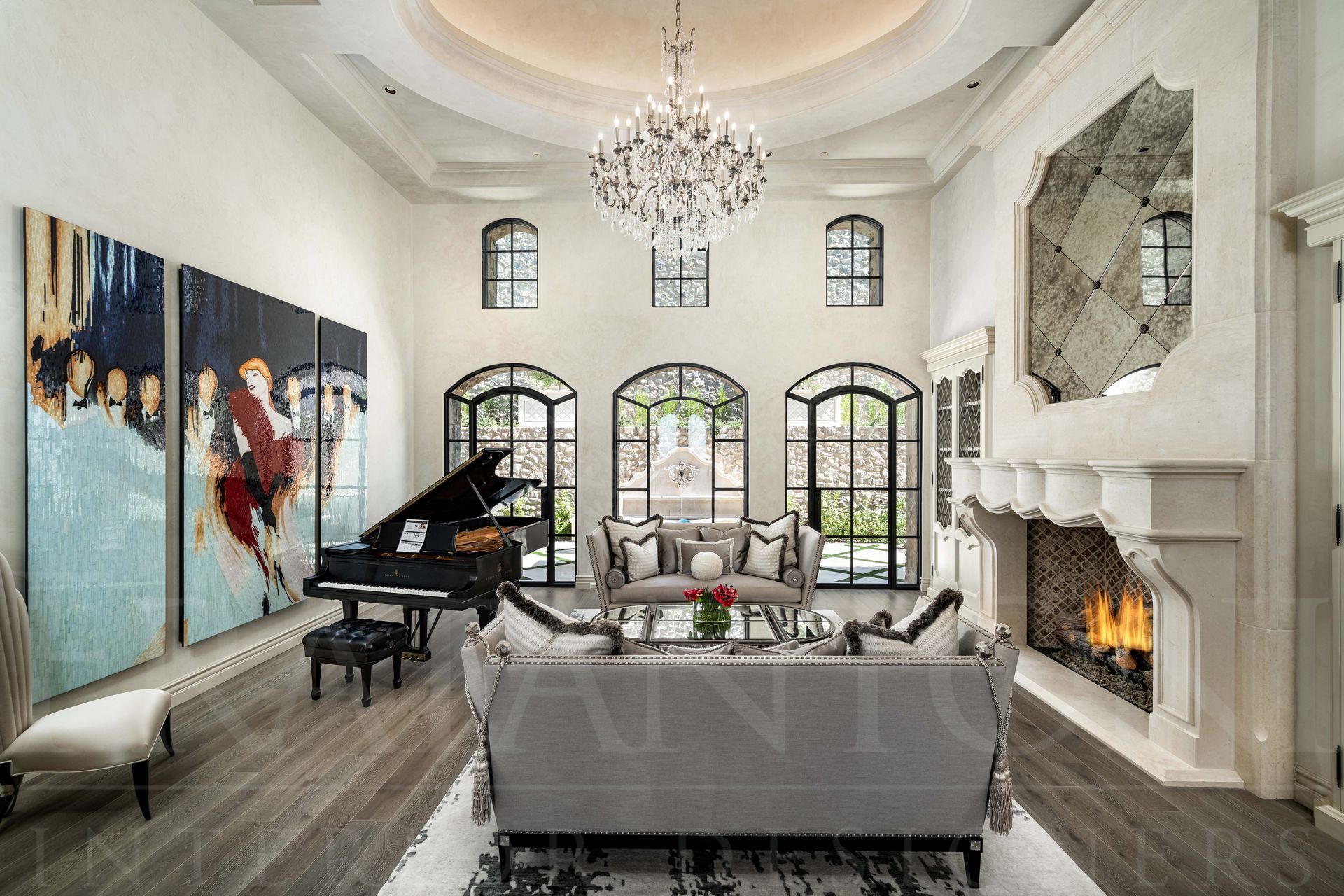 A luxurious, French designed high-ceilinged formal living room with a grand piano, grey sofas, a large custom stone fireplace, and modern wall art.