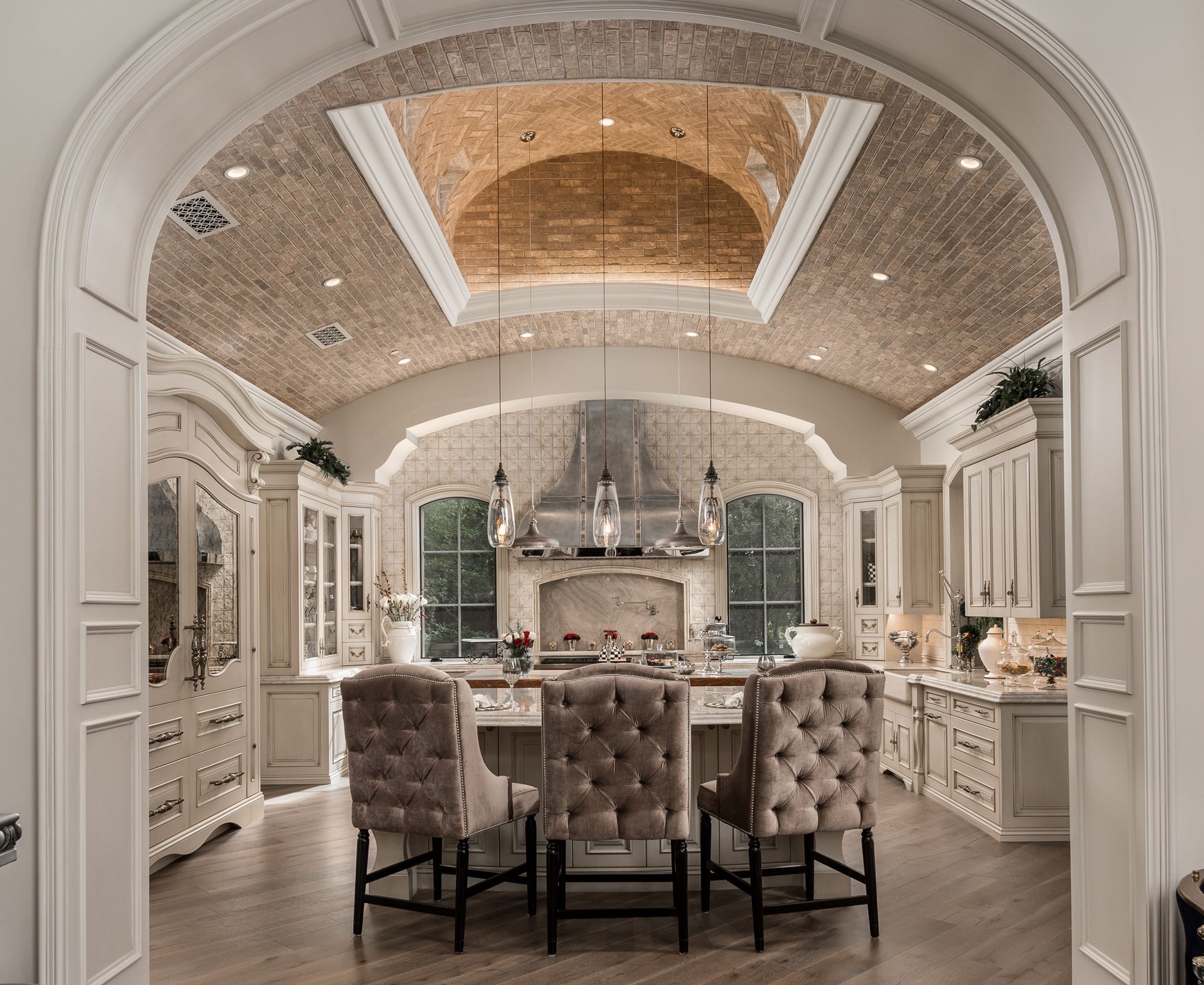 Elegant kitchen with beige cabinets, brick ceiling detail, and three tufted bar stools at an island.