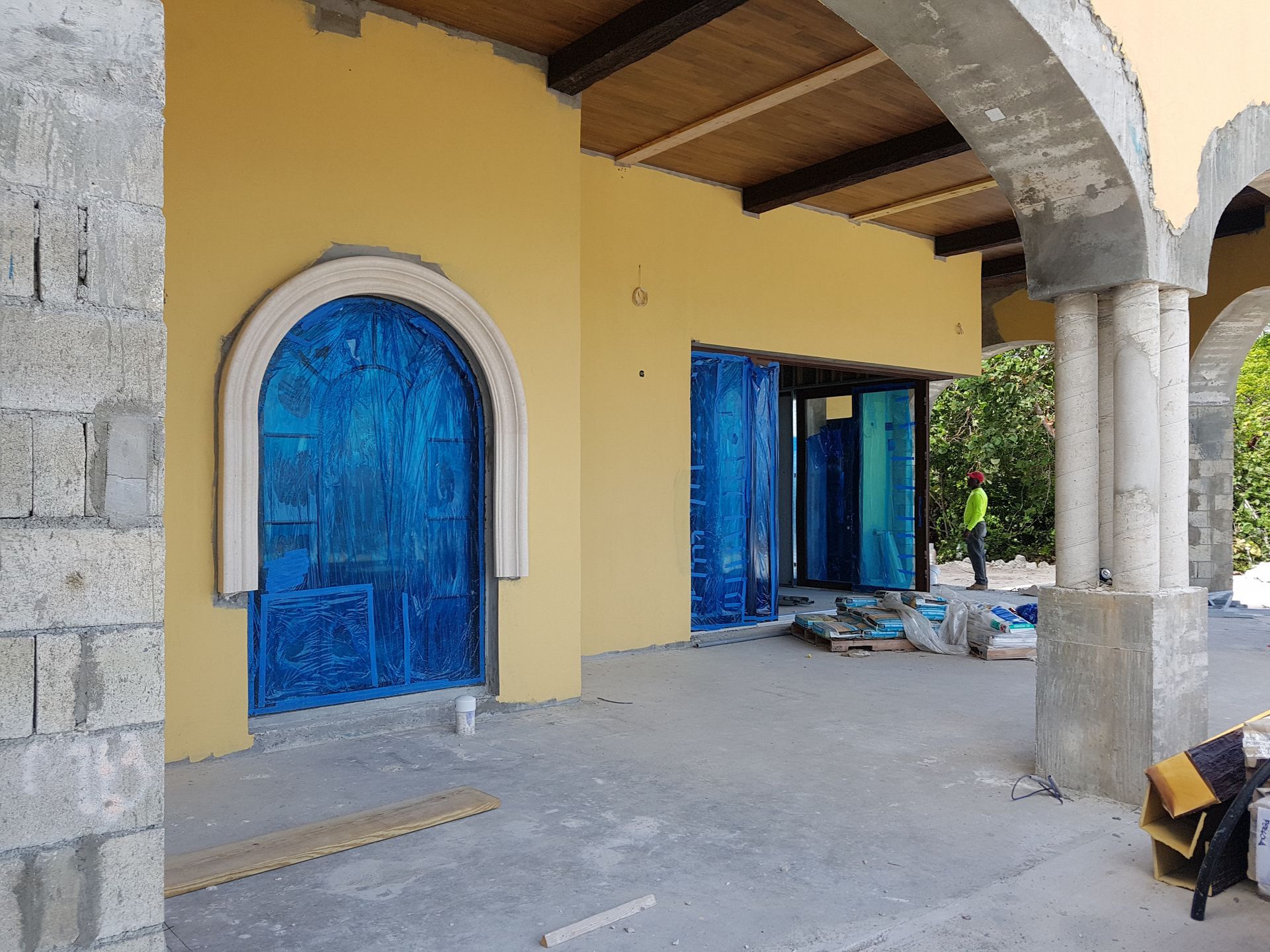 Building exterior under construction with yellow walls, blue-covered doors, and stone pillars.