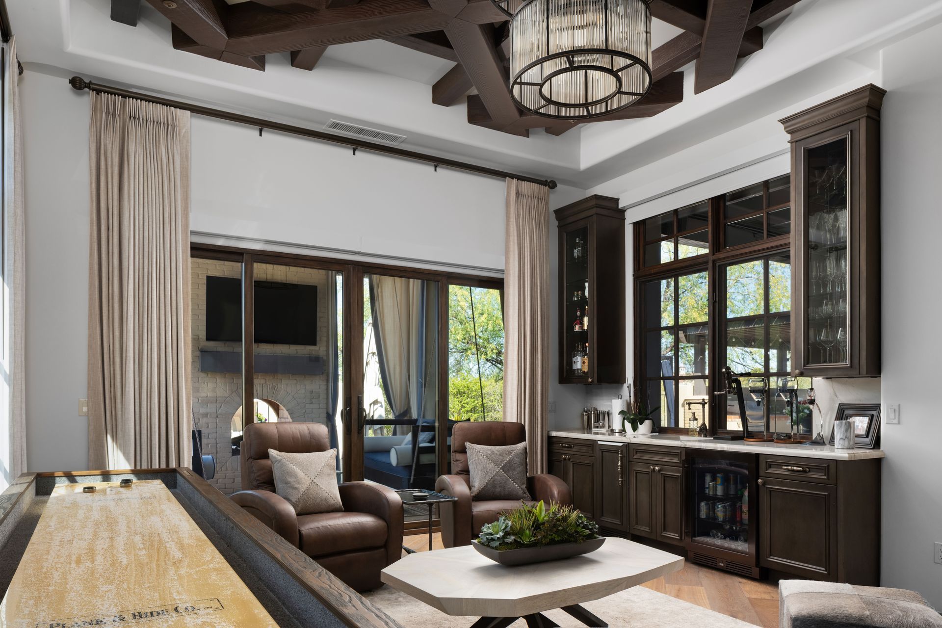 A home bar with brown cabinets, shuffleboard, leather chairs, and sliding doors to a patio.