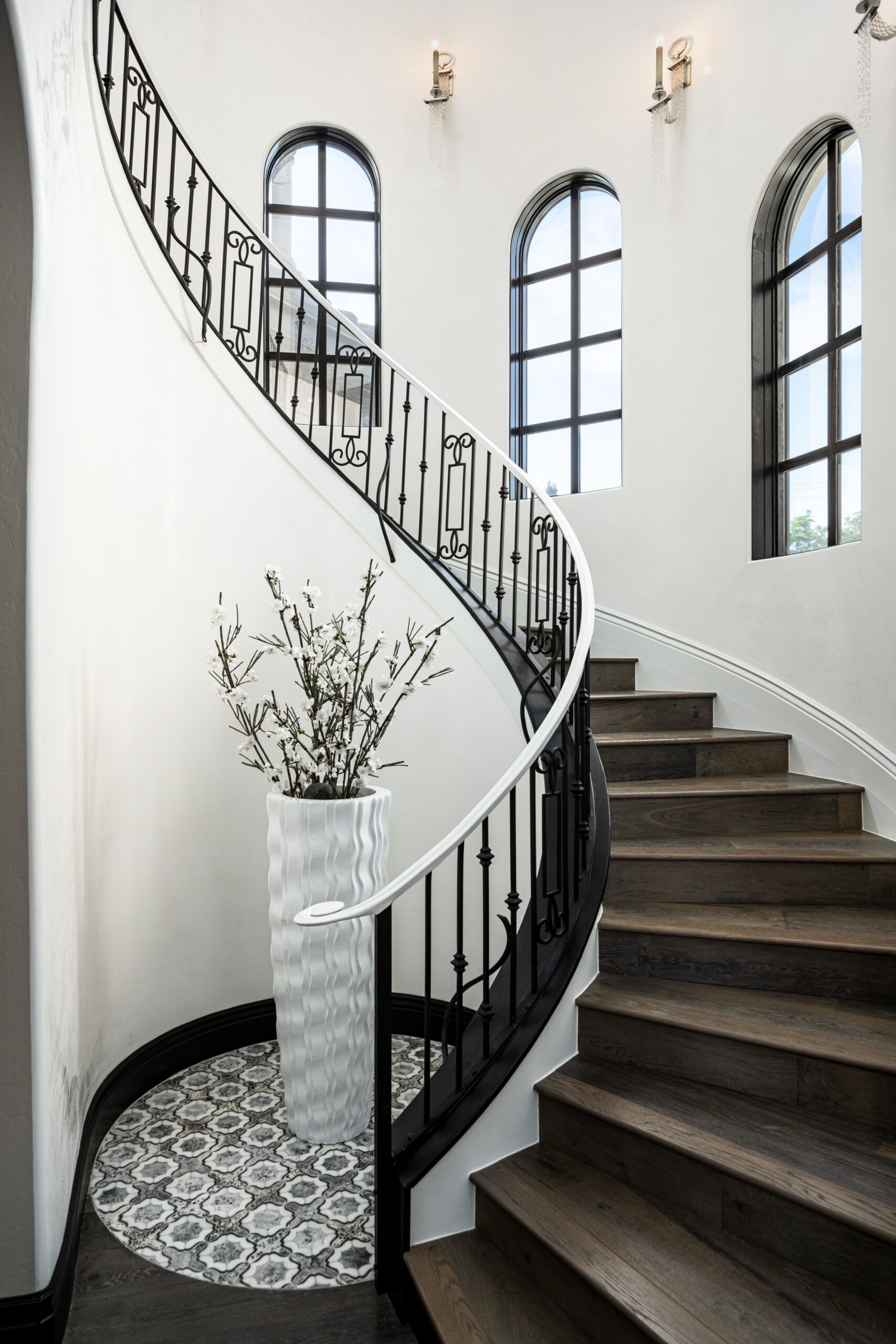 A spiral staircase with a wrought iron railing and a vase of flowers on the bottom.