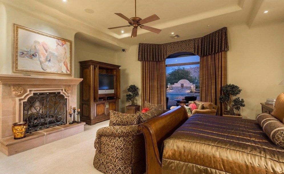 A bedroom with a large bed , fireplace , television and ceiling fan.