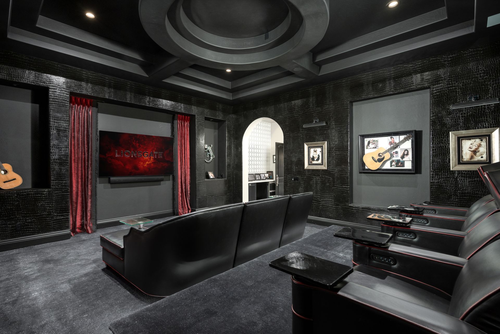 Dark-themed home theater with black leather seating, a large screen, and a starry floor. Red curtains and decorative art.