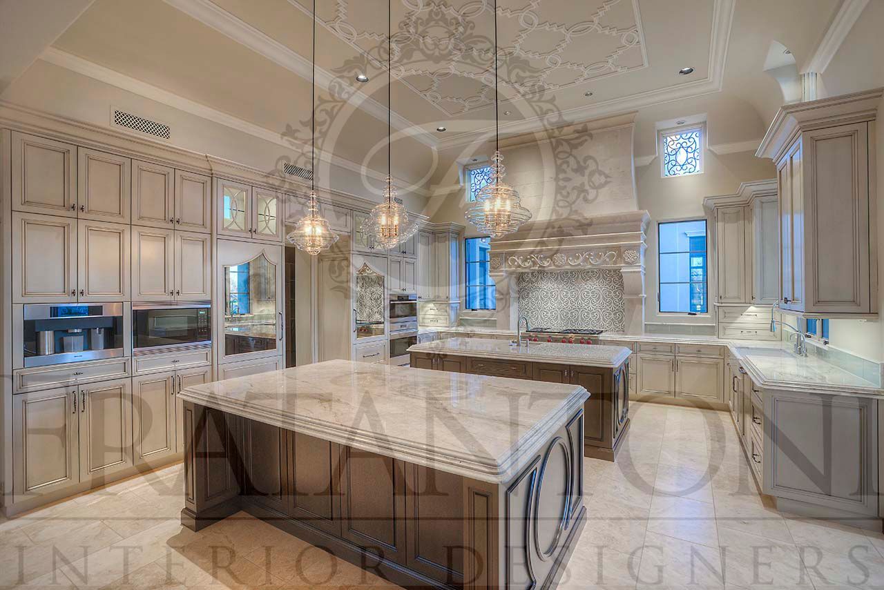 Elegant neutral luxury kitchen with marble double islands, ornate cabinetry, custom range hood, glass pendant lights, and a custom paneled fridge