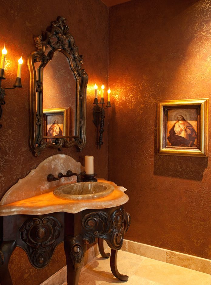 Elegant powder room with ornate vanity, mirror, and sconces; warm brown walls, artwork, and gold accents.
