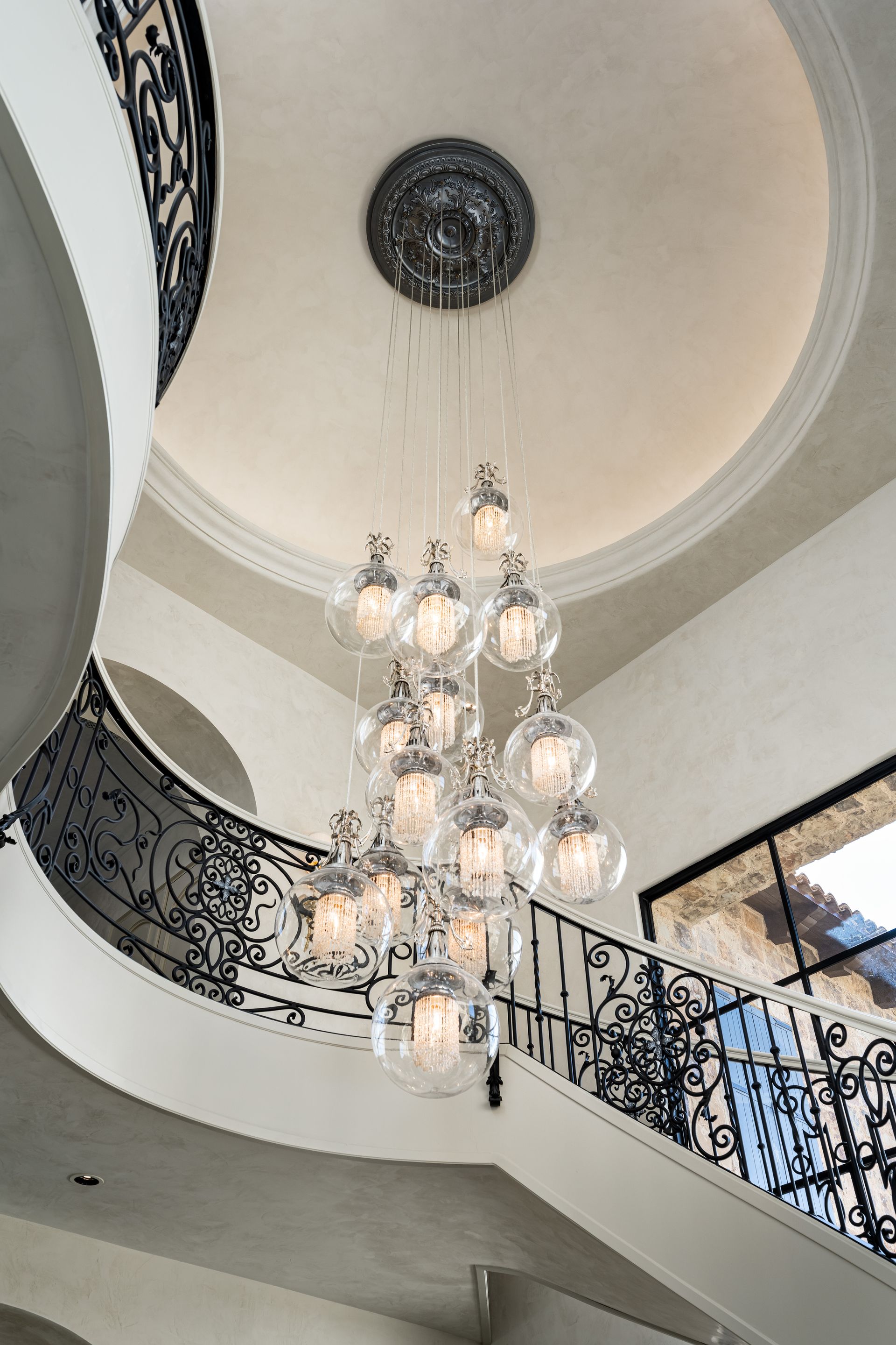 Ornate chandelier hanging in a two-story foyer with a curved staircase.