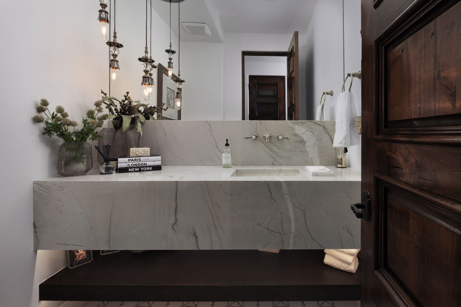 Bathroom with stone countertop and dark wood door. Overhead lights and mirror.