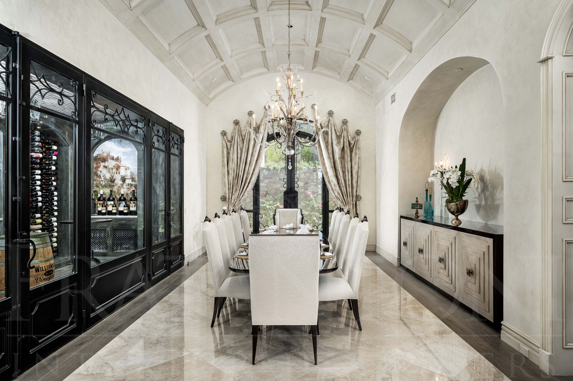 A formal French style, dining room, custom white chairs, a coffered vaulted ceiling, and a glass-walled wine cellar designed by Fratantoni Interior Designers