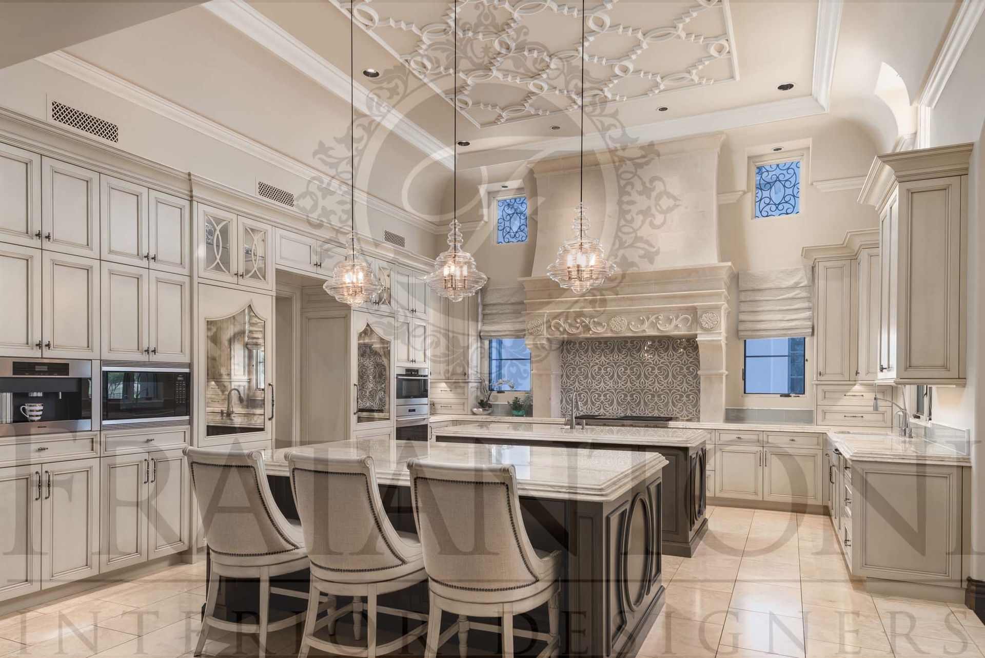 Elegant neutral luxury kitchen with double islands, bar stools, ornate glass pendant lights, detailed tall ceilings, a custom range hood, and natural stone floors