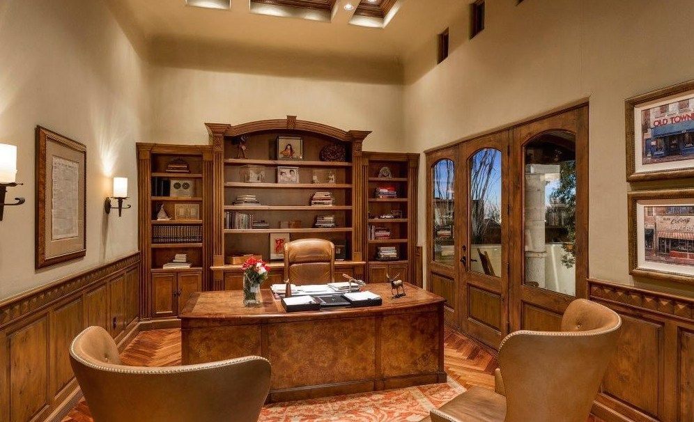 A home office with a desk , chairs and shelves.