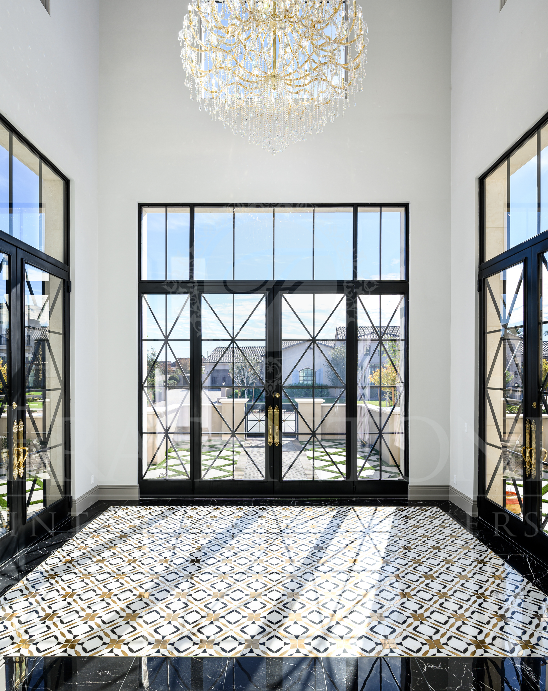 Elegant modern entry with tall black-framed windows, white walls, crystal chandelier, and a mosaic tile floor.