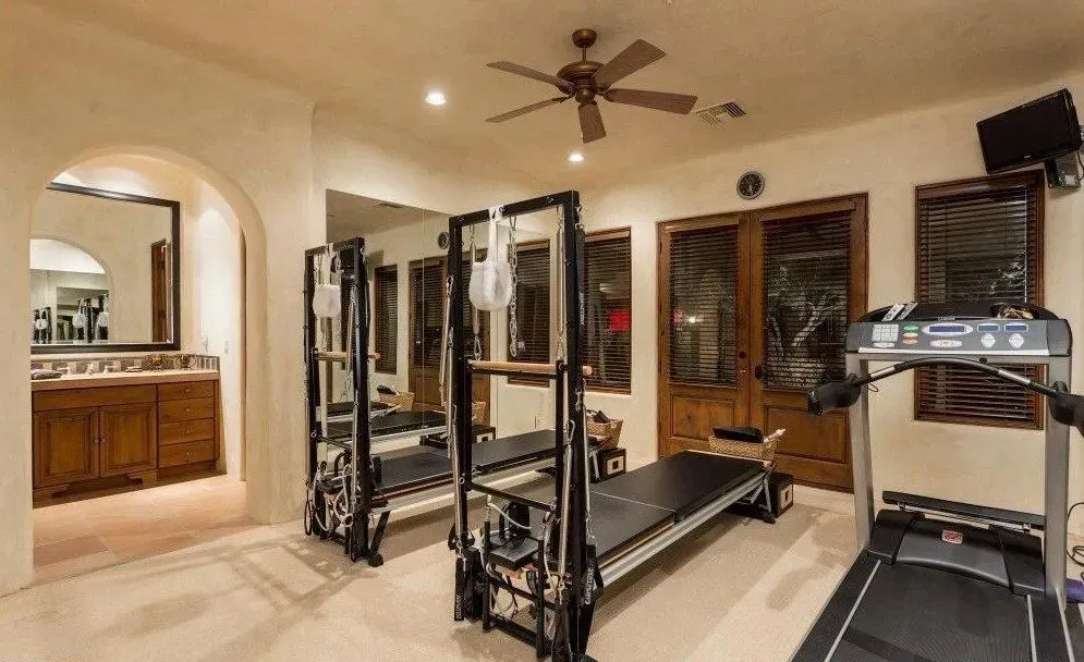 Home gym with Pilates reformer, treadmill, mirrors, and doorway leading to bathroom.