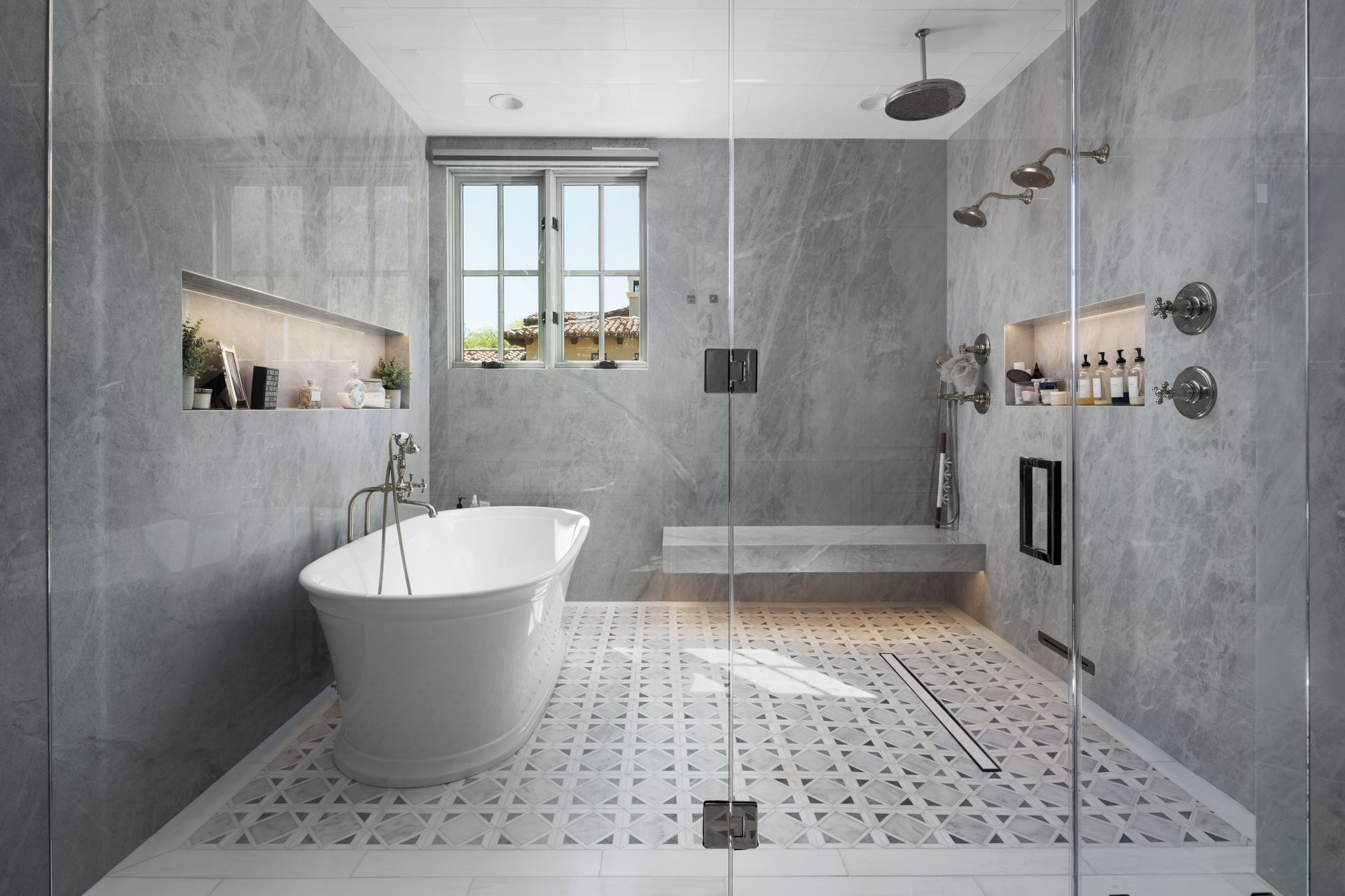 Modern bathroom with gray tile, freestanding tub, walk-in shower, and window.