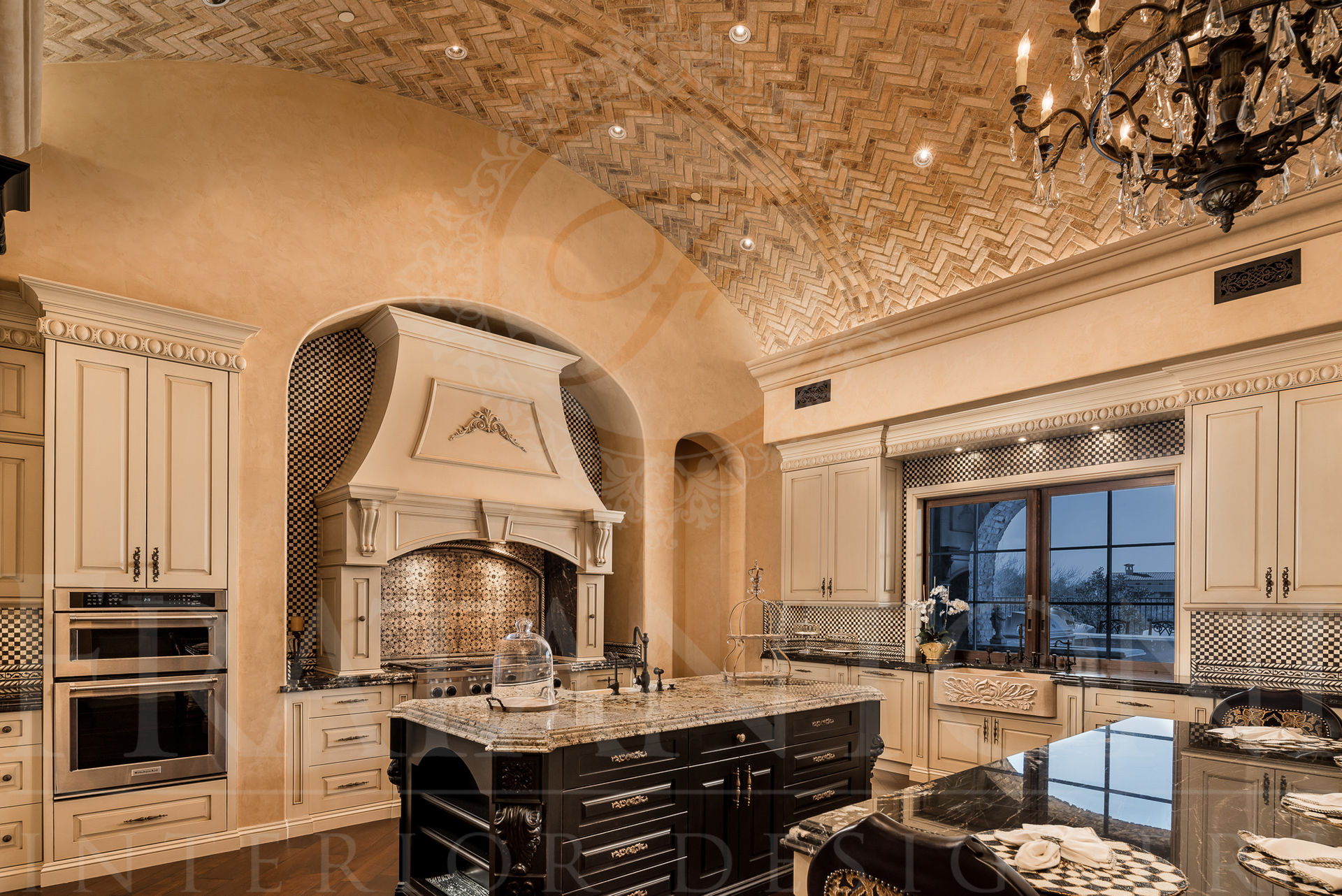 Luxurious kitchen with arched ceiling, ornate cabinets, dark granite island, and chandelier.
