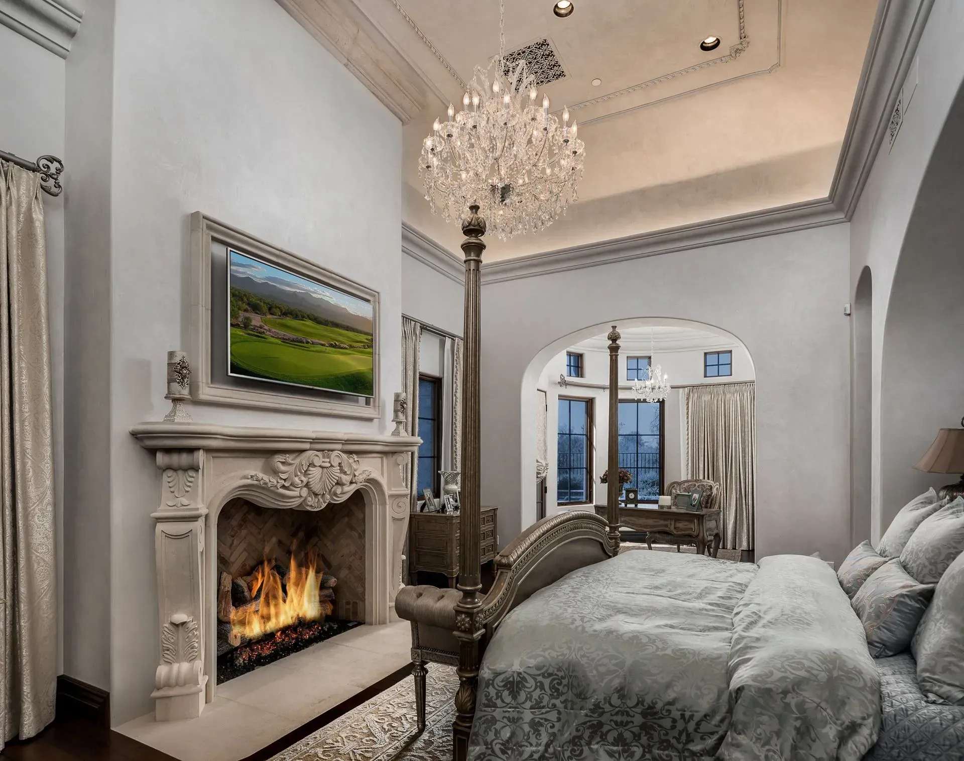 Luxurious bedroom with fireplace, four-poster bed, chandelier, and a TV above the fireplace.