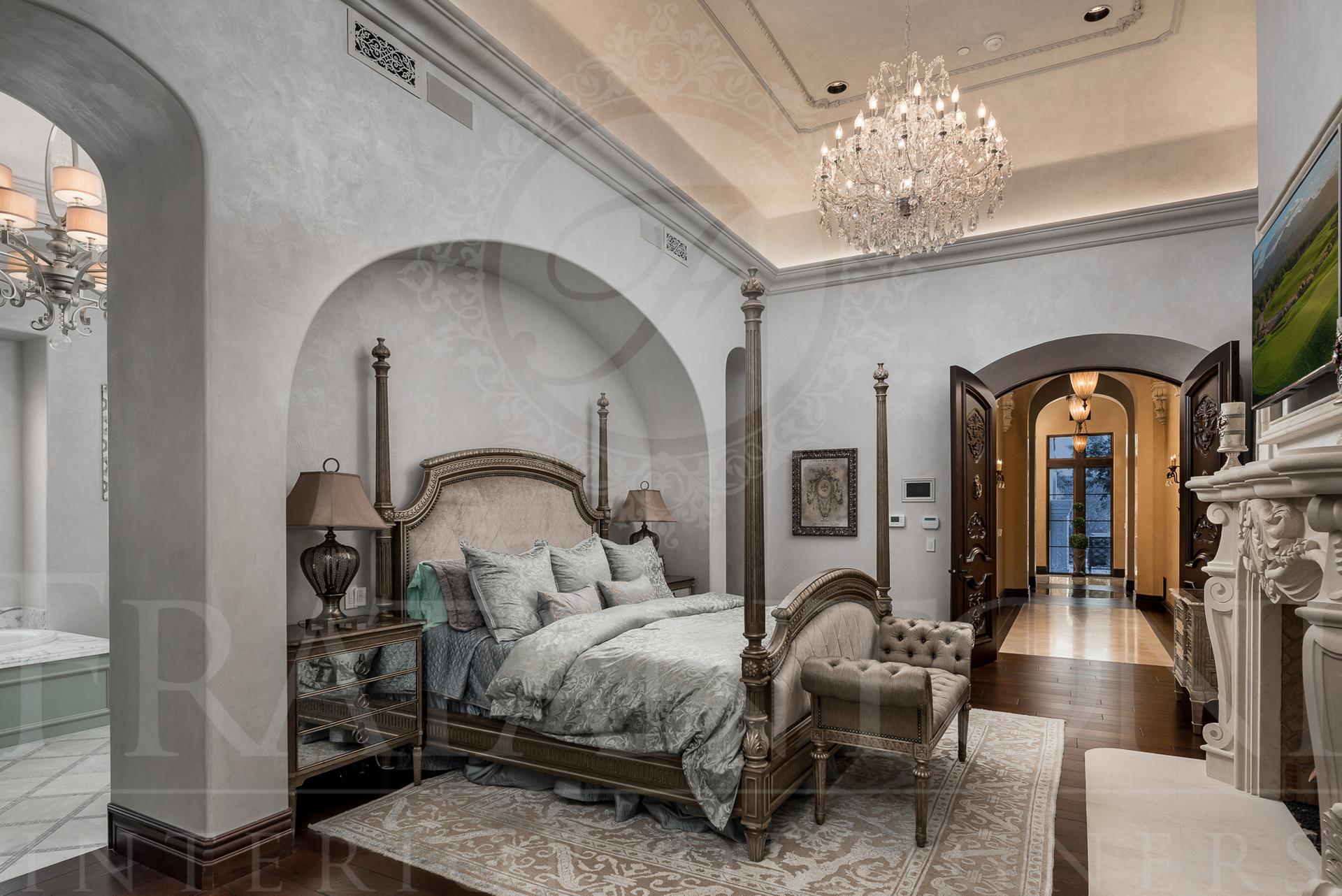 Elegant bedroom with four-poster bed, chandelier, and arched doorway leading to hallway and outside.