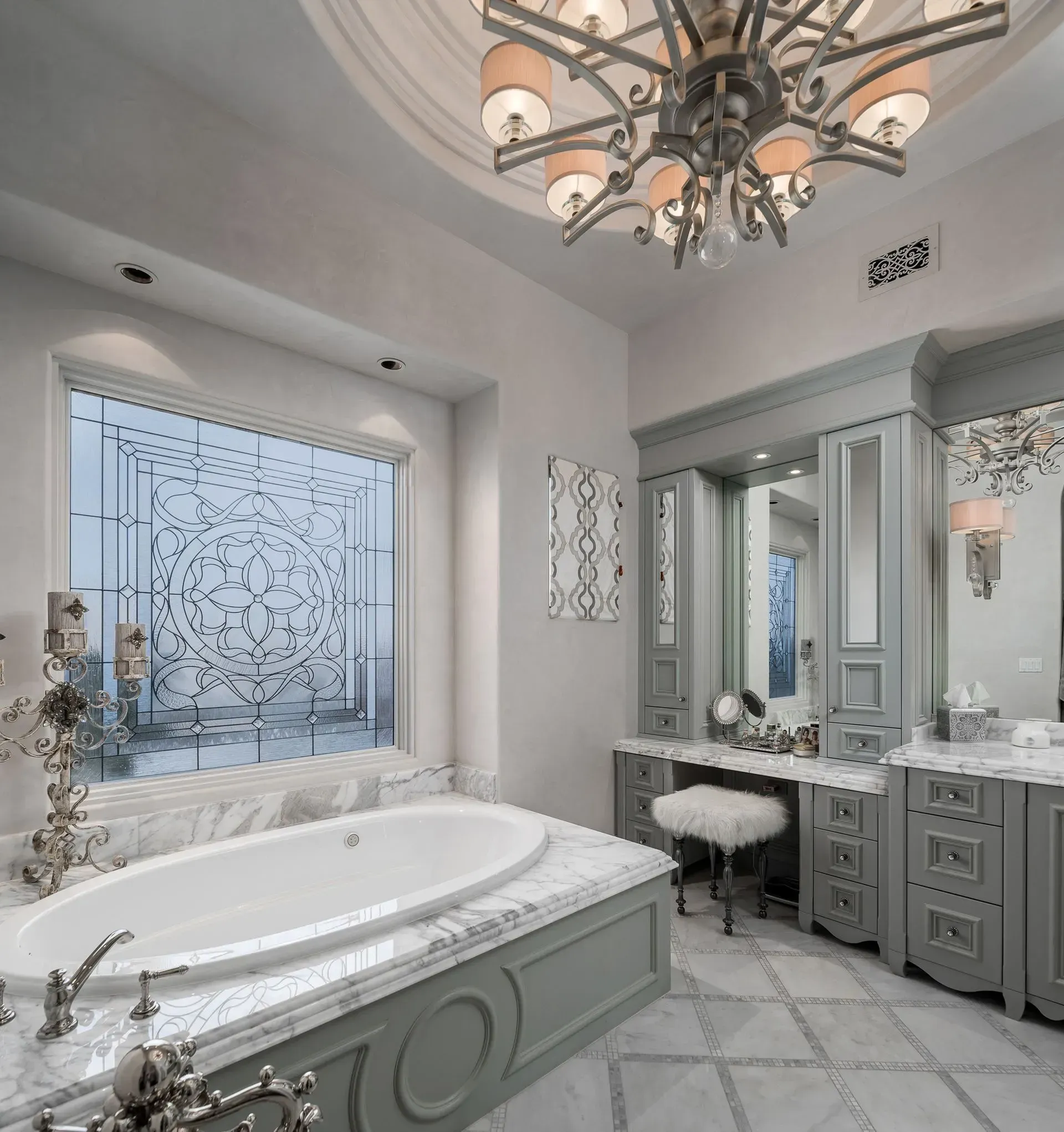 Luxurious bathroom with oval tub, gray vanity, and ornate chandelier.