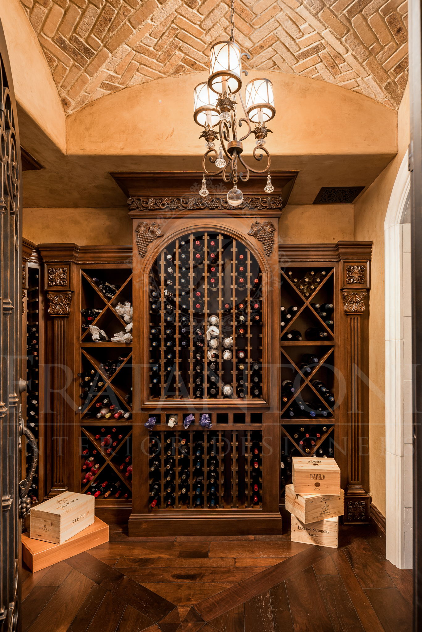 Wine cellar with wooden racks, ornate cabinet, brick ceiling, and chandelier.