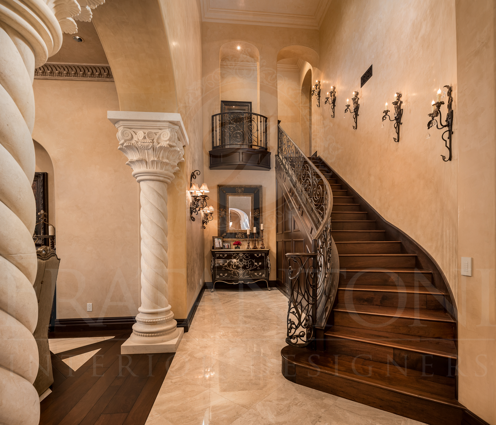 Elegant foyer with marble floor, winding staircase, decorative wrought iron railing, and ornate columns.
