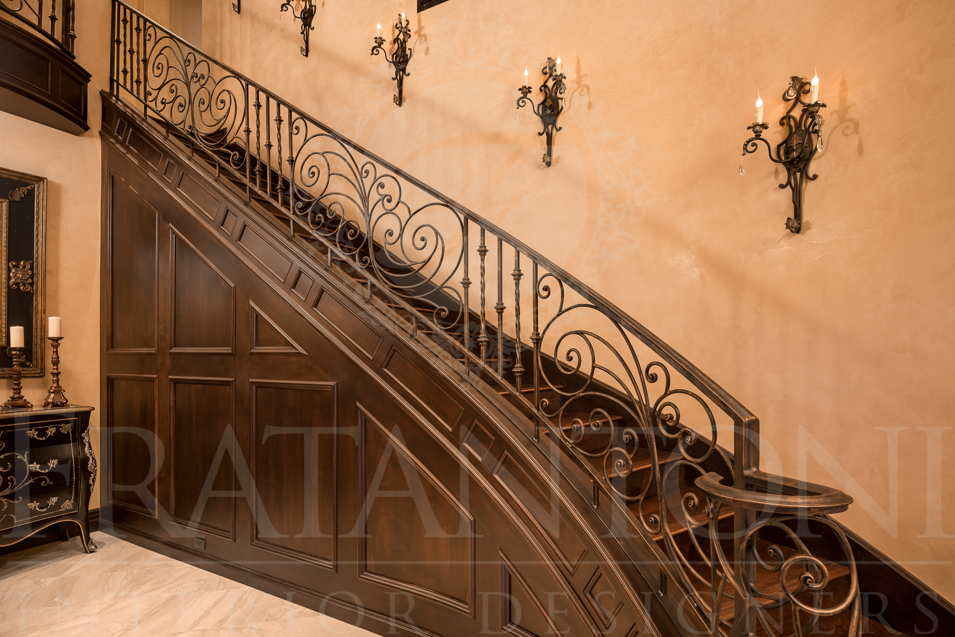Ornate wrought iron staircase with decorative railing, dark wood panels, and wall sconces.