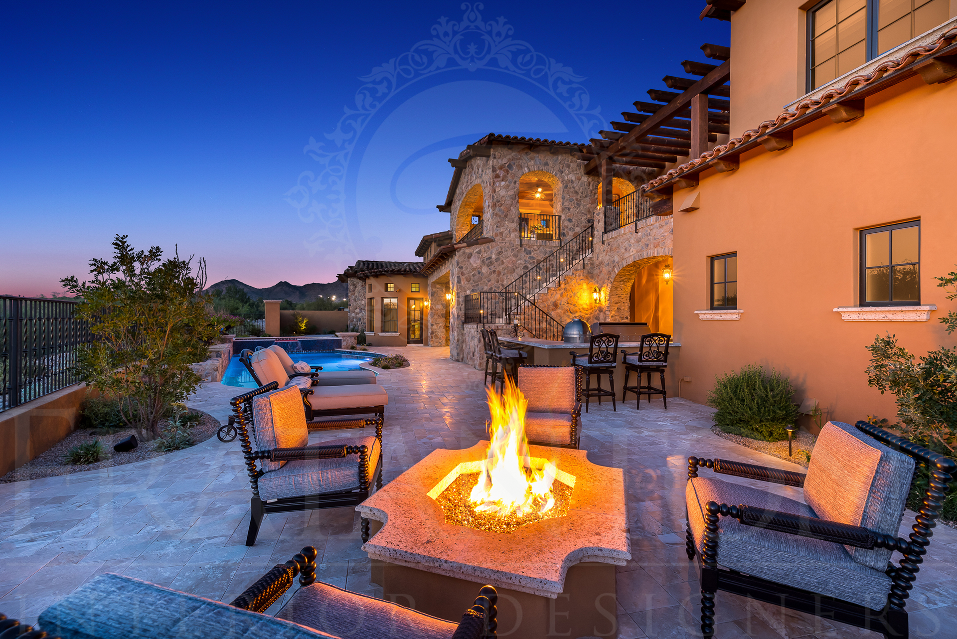 Outdoor patio with fire pit, seating, pool, and a luxury home at twilight.