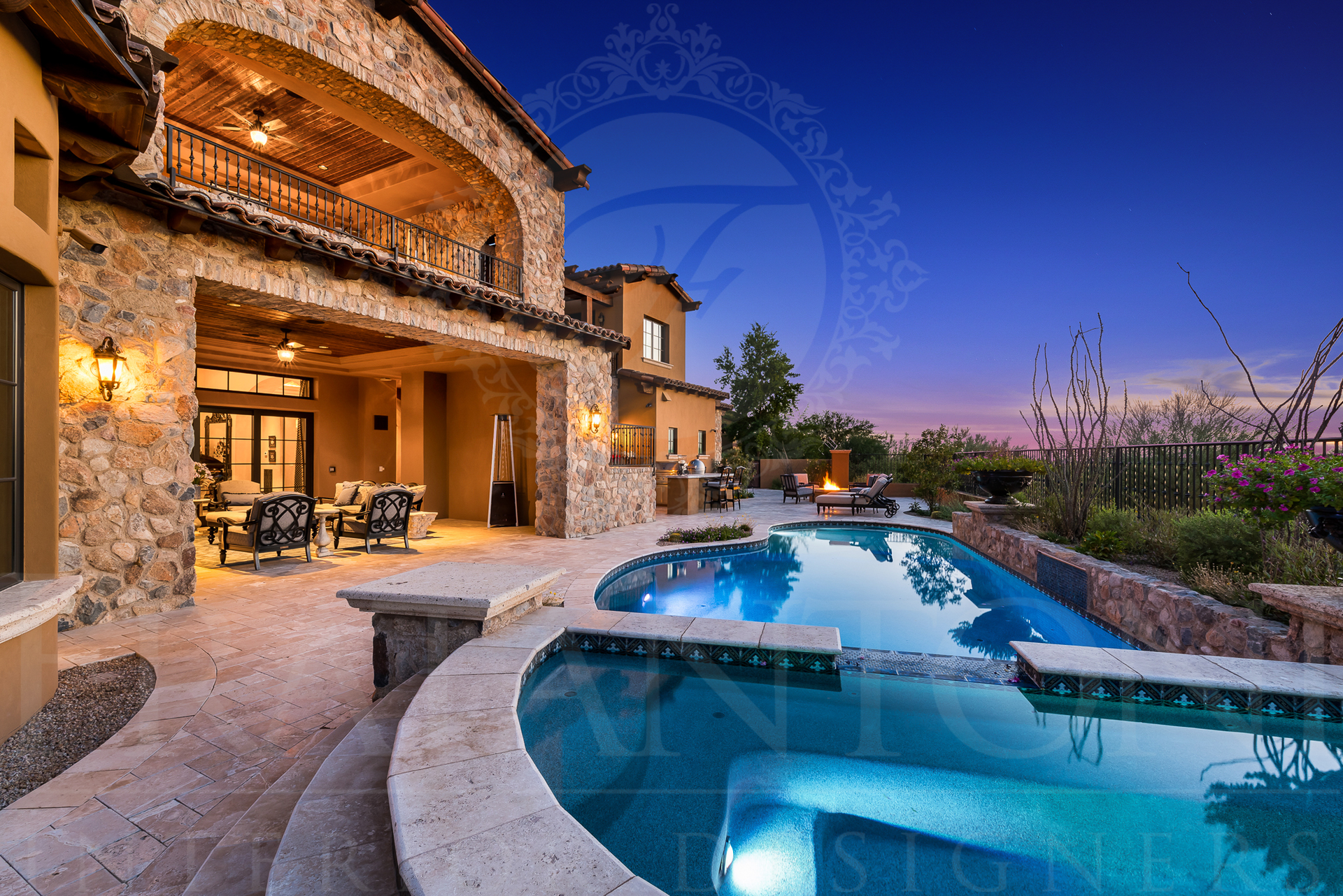 Luxury home with a pool at dusk; stone exterior, patio with seating, balcony, and dark blue pool.