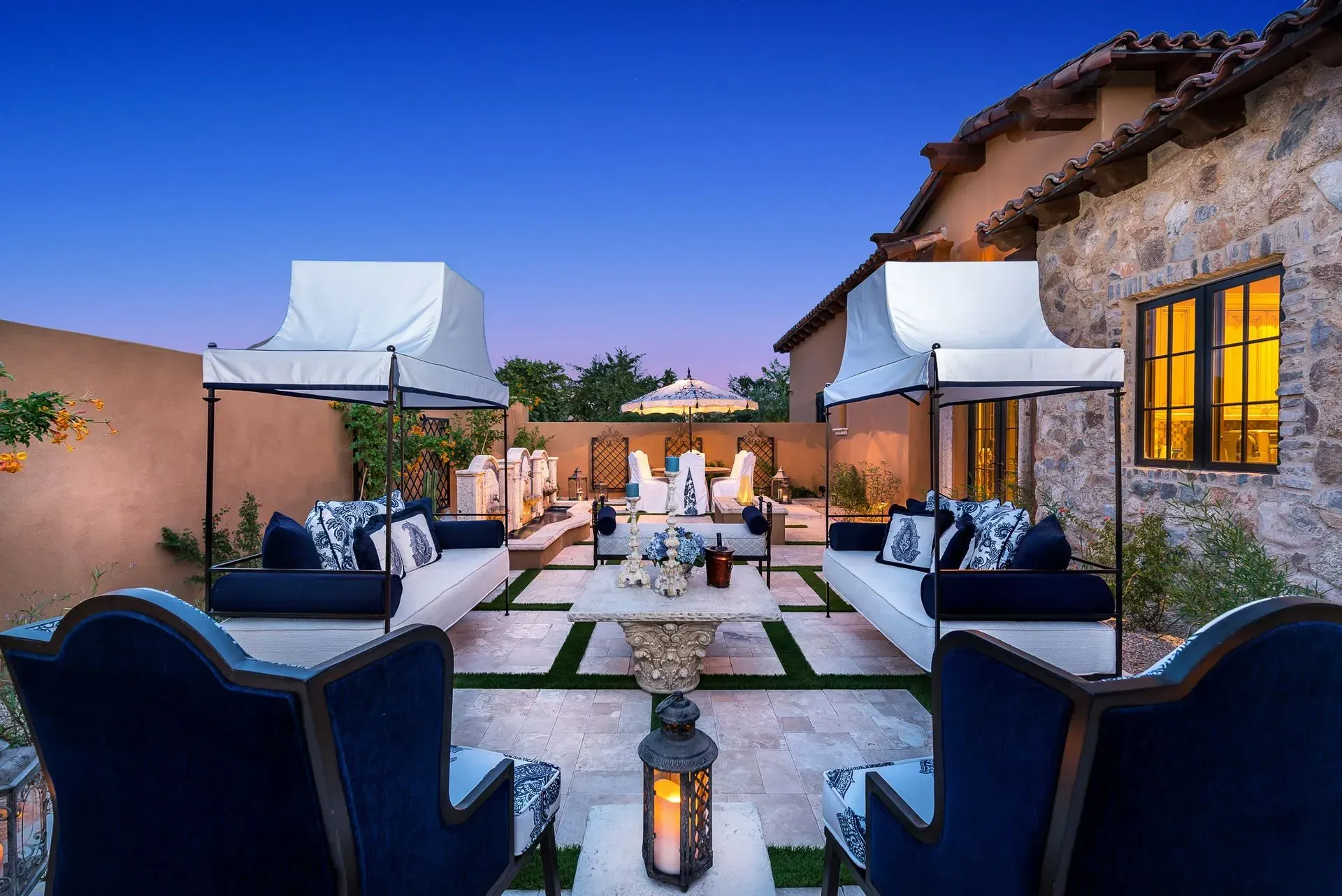 Outdoor lounge area with navy and white furniture, stone walls, and evening sky.