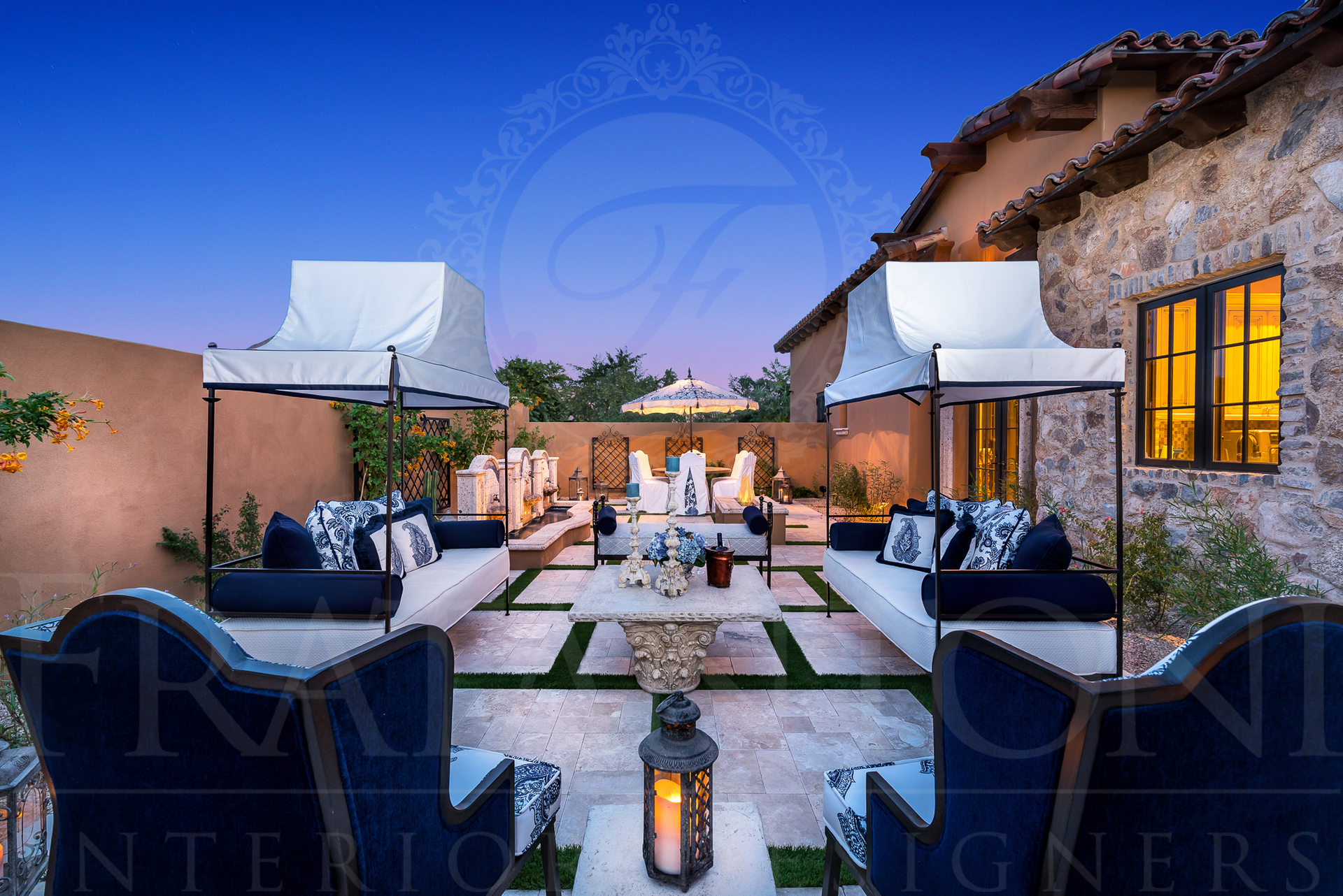 Outdoor patio with lounge furniture under canopies at dusk. Stone walls and lawn.