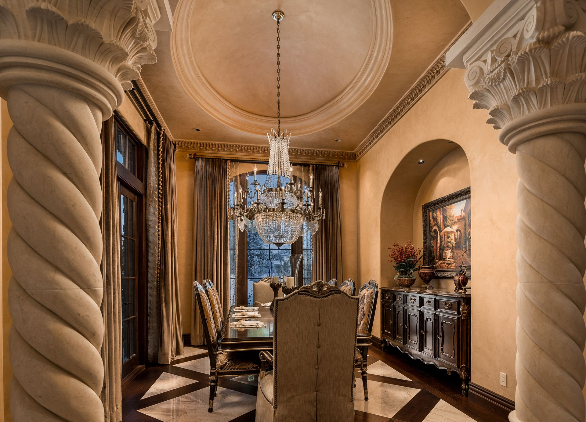 Elegant dining room with chandelier, ornate columns, and dark wood furniture.