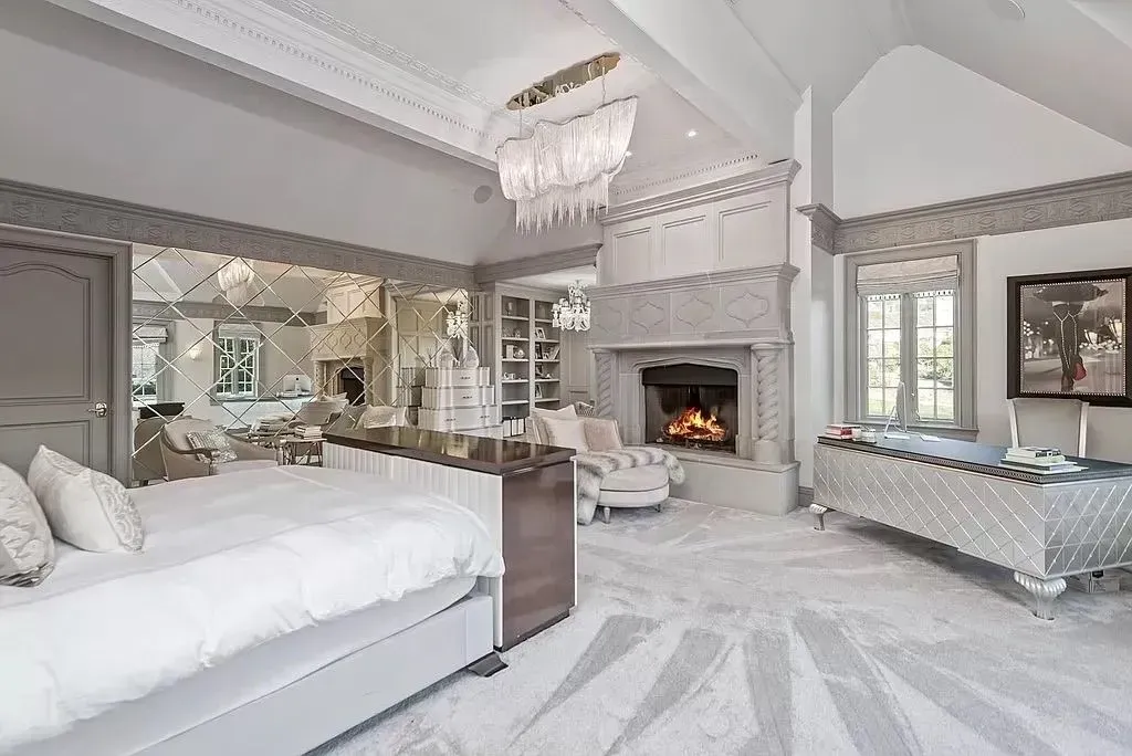 Luxurious bedroom with fireplace, chandelier, mirrored wall, and plush gray carpet.