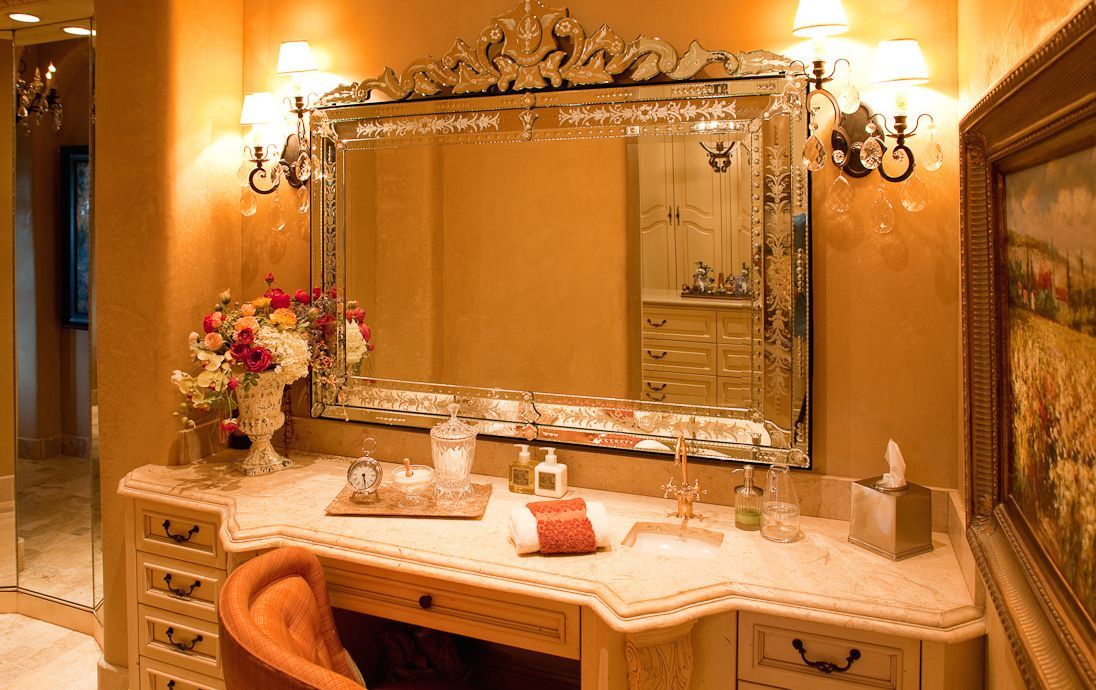Vanity with mirror, flowers, and cosmetics. Ornate mirror frame, gold and cream decor.