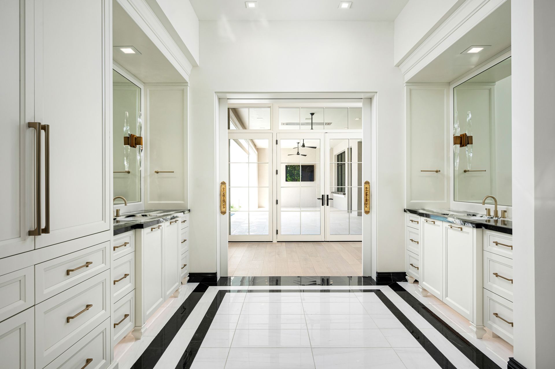 White and black bathroom with dual sinks, mirrors, and glass doors leading to another room.